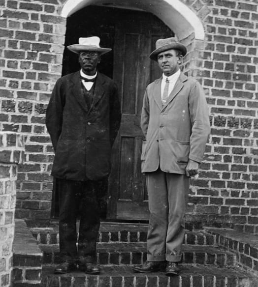 A formal portrait of John Chilembwe in a dark suit and hat