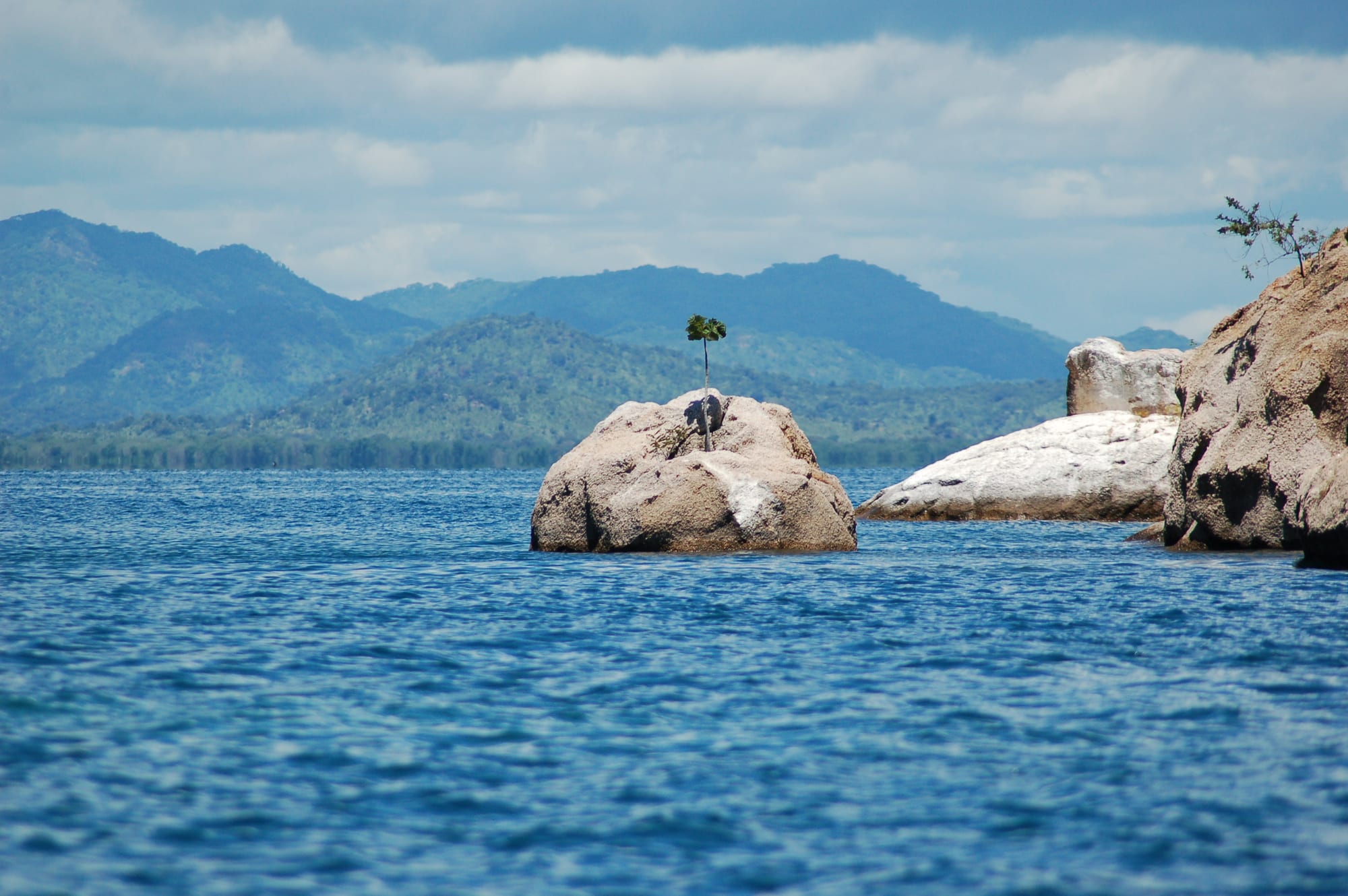 A calm bay of Lake Malawi with wooded hills and a fishing canoe on clear water