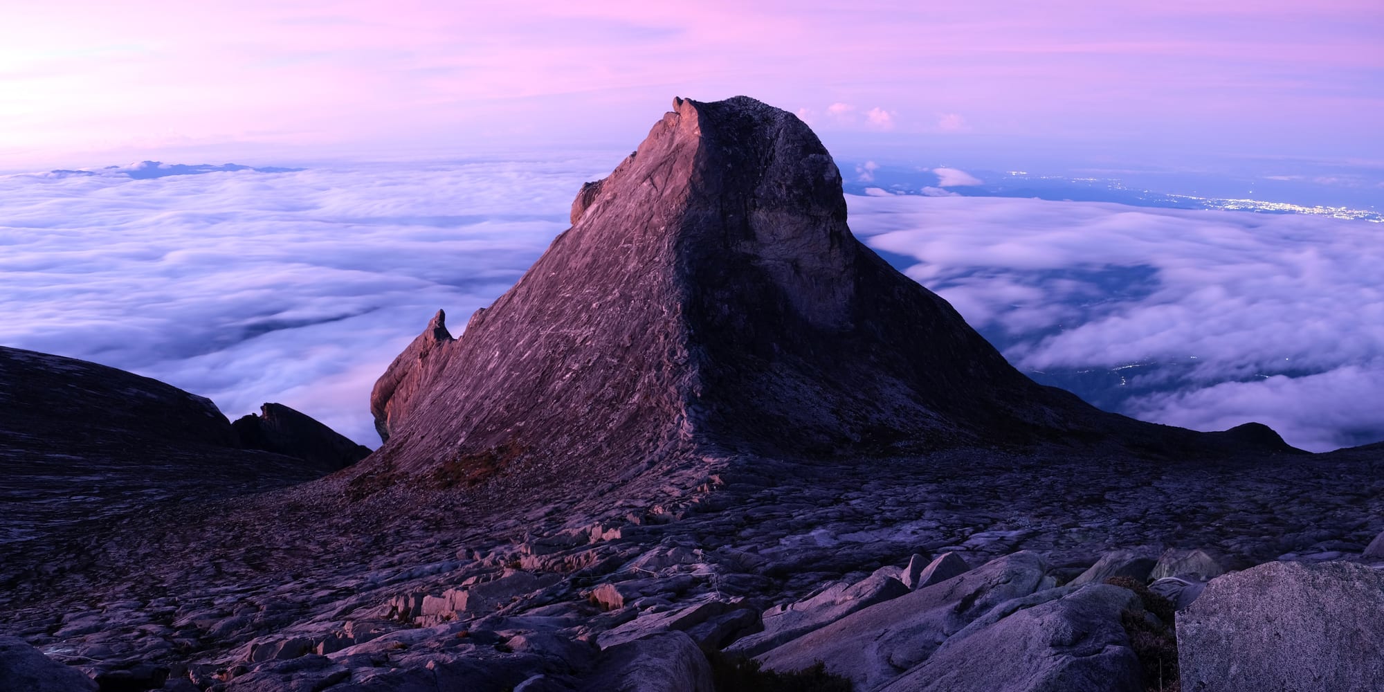 A massive bare granite mountain summit rising above cloud and forest