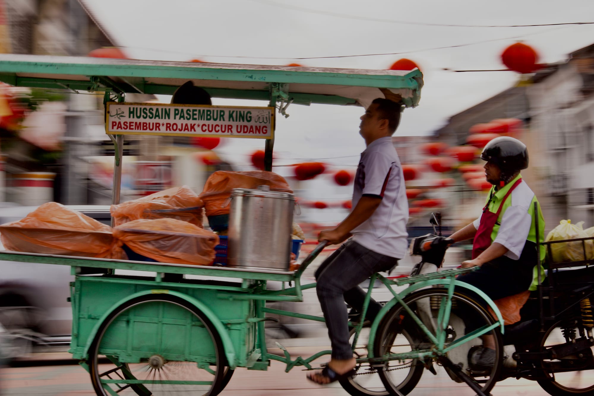 A street food vendor riding a tricycle cart through a busy street