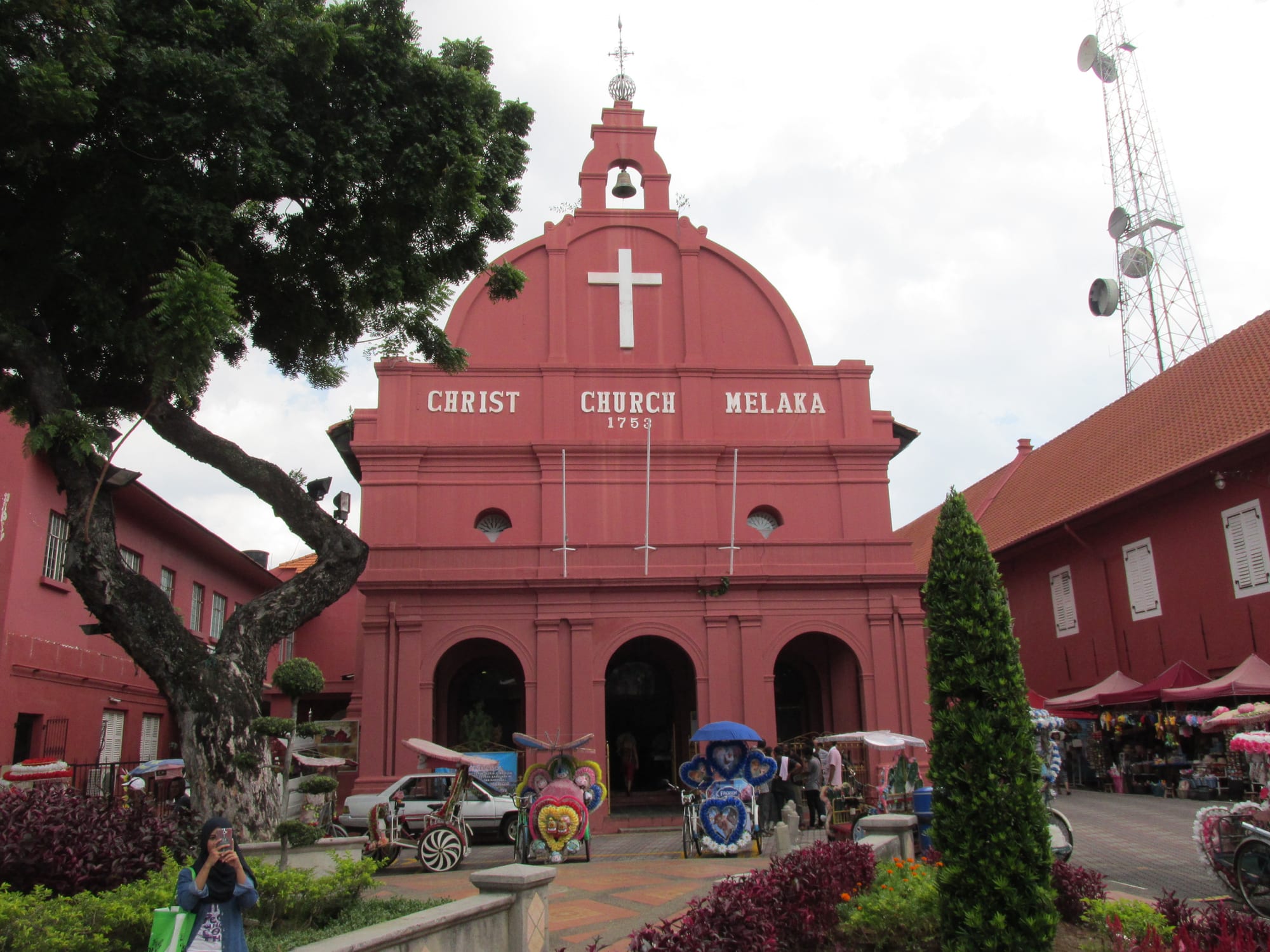 A red-painted Dutch colonial church and clock tower on Malacca's Dutch Square with cycle rickshaws