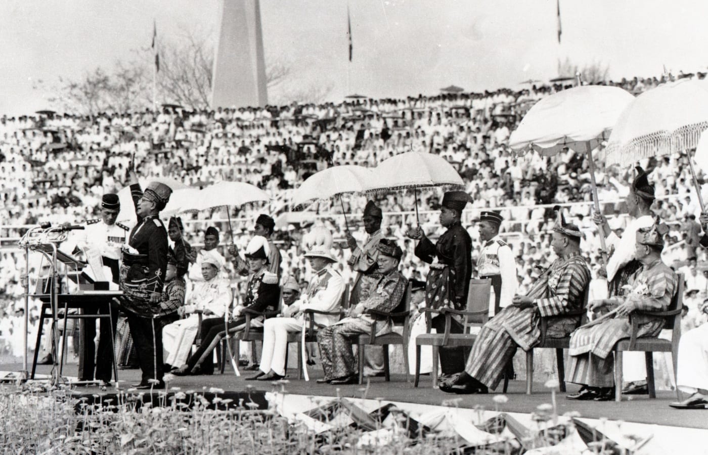 Tunku Abdul Rahman reading the independence proclamation before a crowd in a stadium in 1957