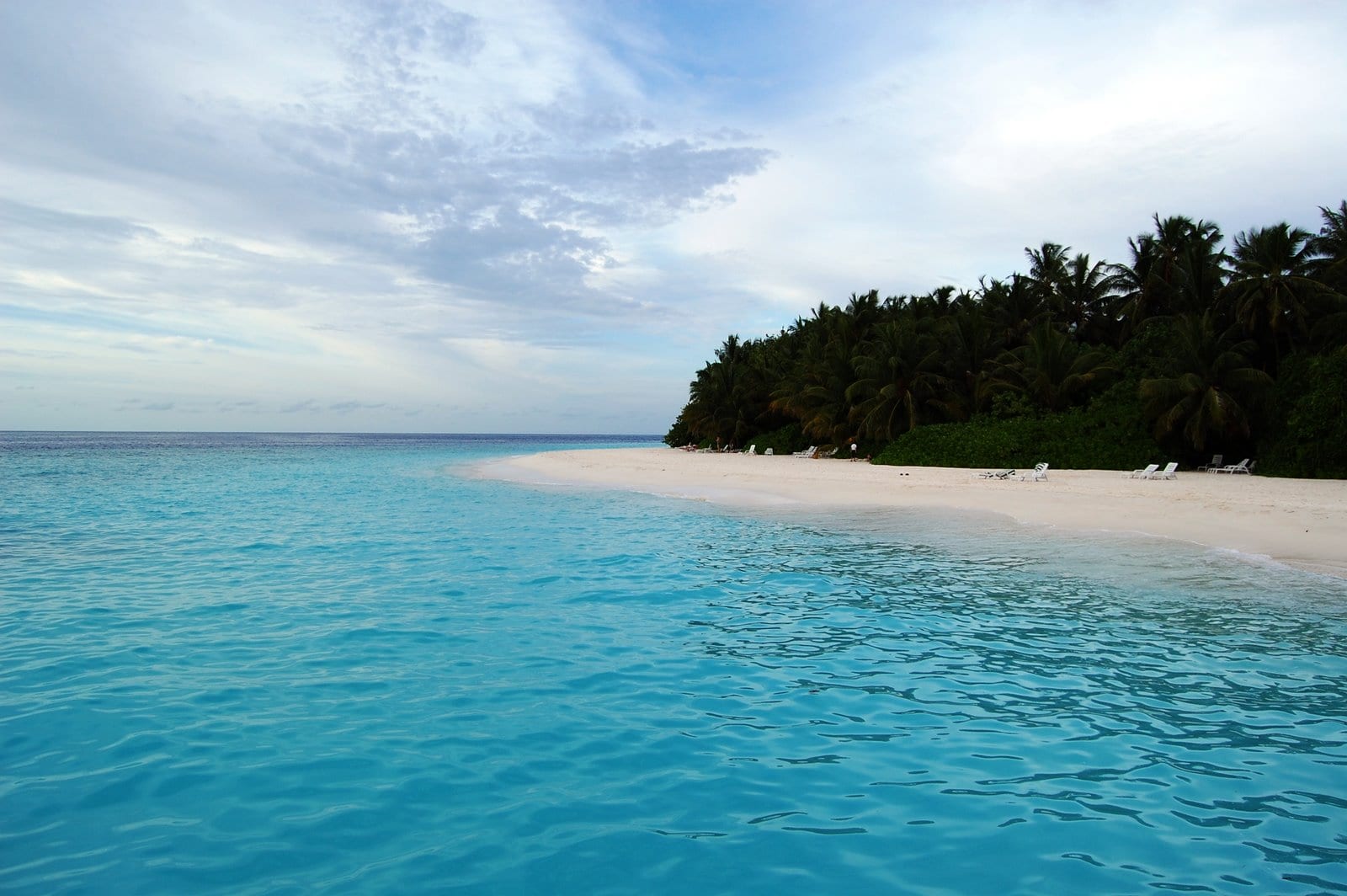 A shallow reef flat with coral visible through clear water beside a white beach