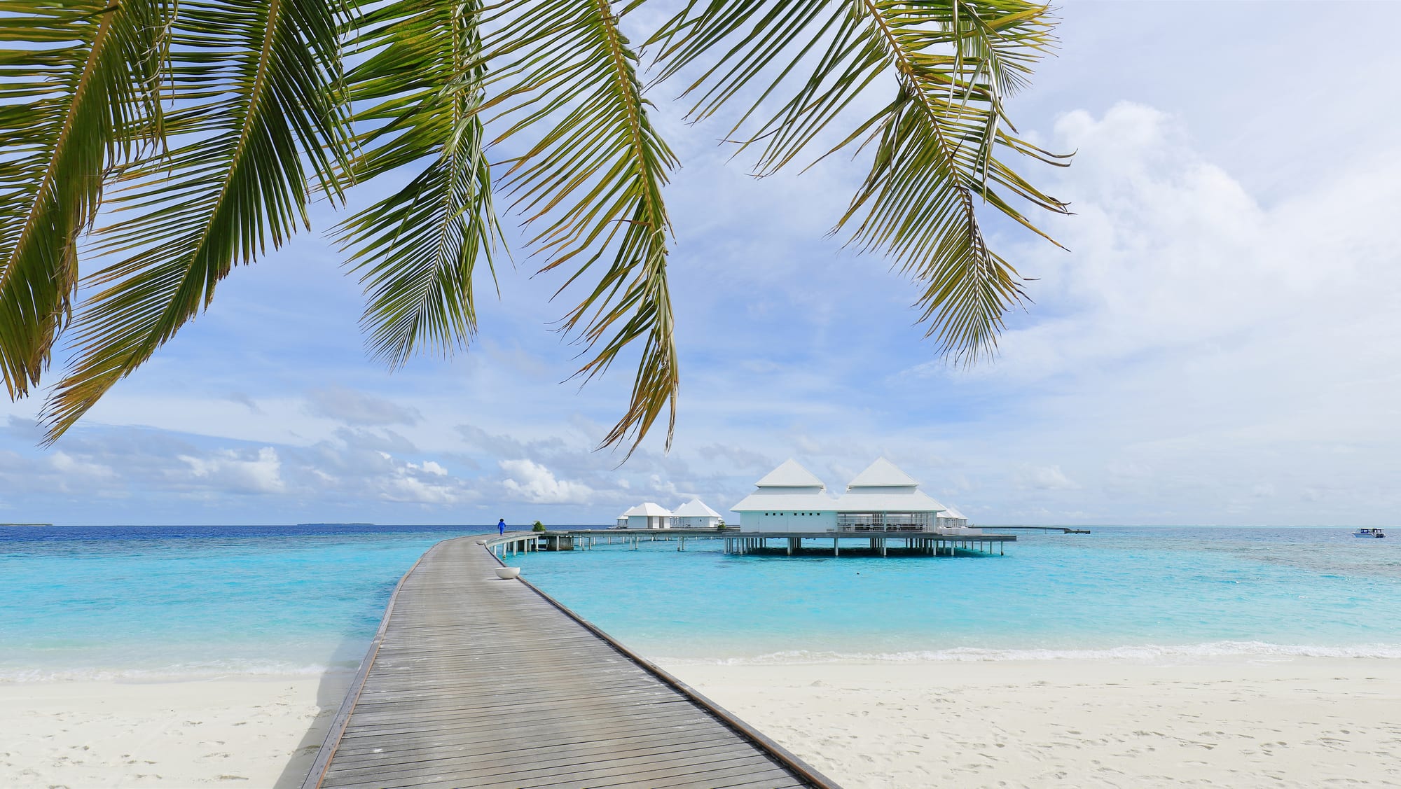 Small overwater bungalows on stilts extending into a shallow turquoise lagoon