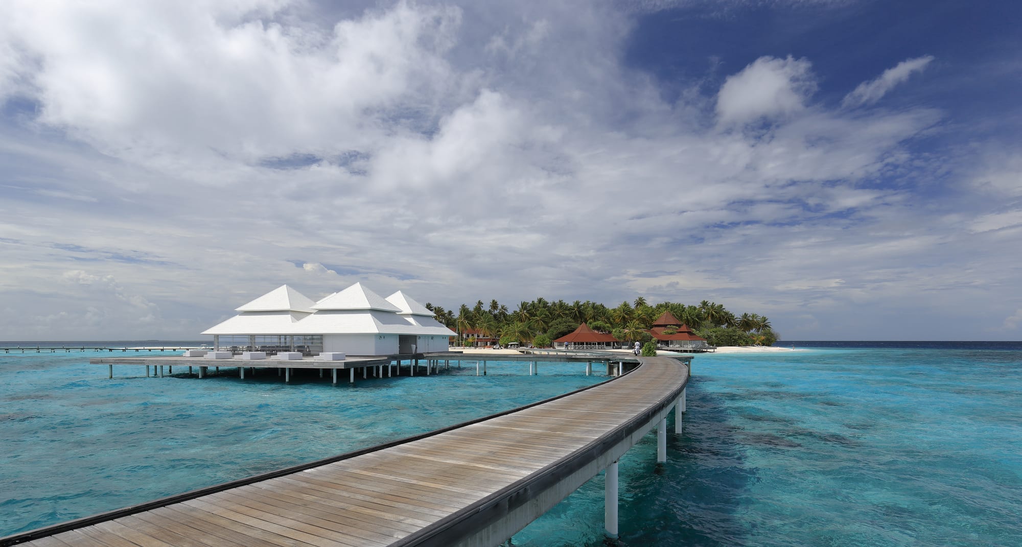 A row of thatched-roof huts on stilts over a clear turquoise lagoon