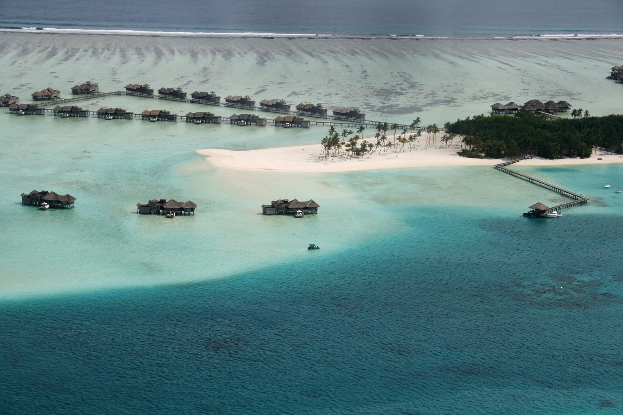 An aerial view of a turquoise lagoon and a thin ring of palm-covered coral islands in deep ocean