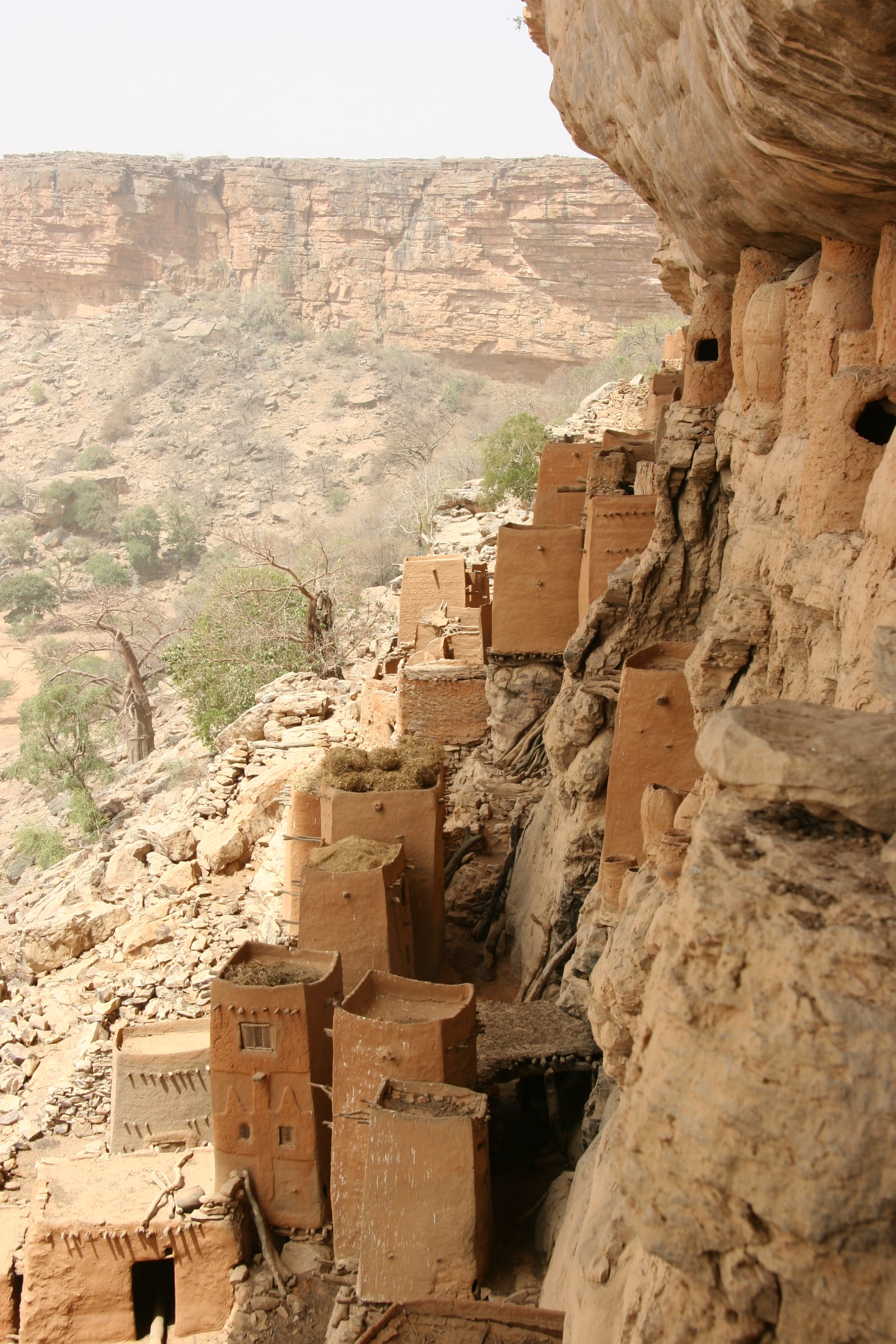 A long sandstone cliff face rising above a flat plain, with small structures at its base