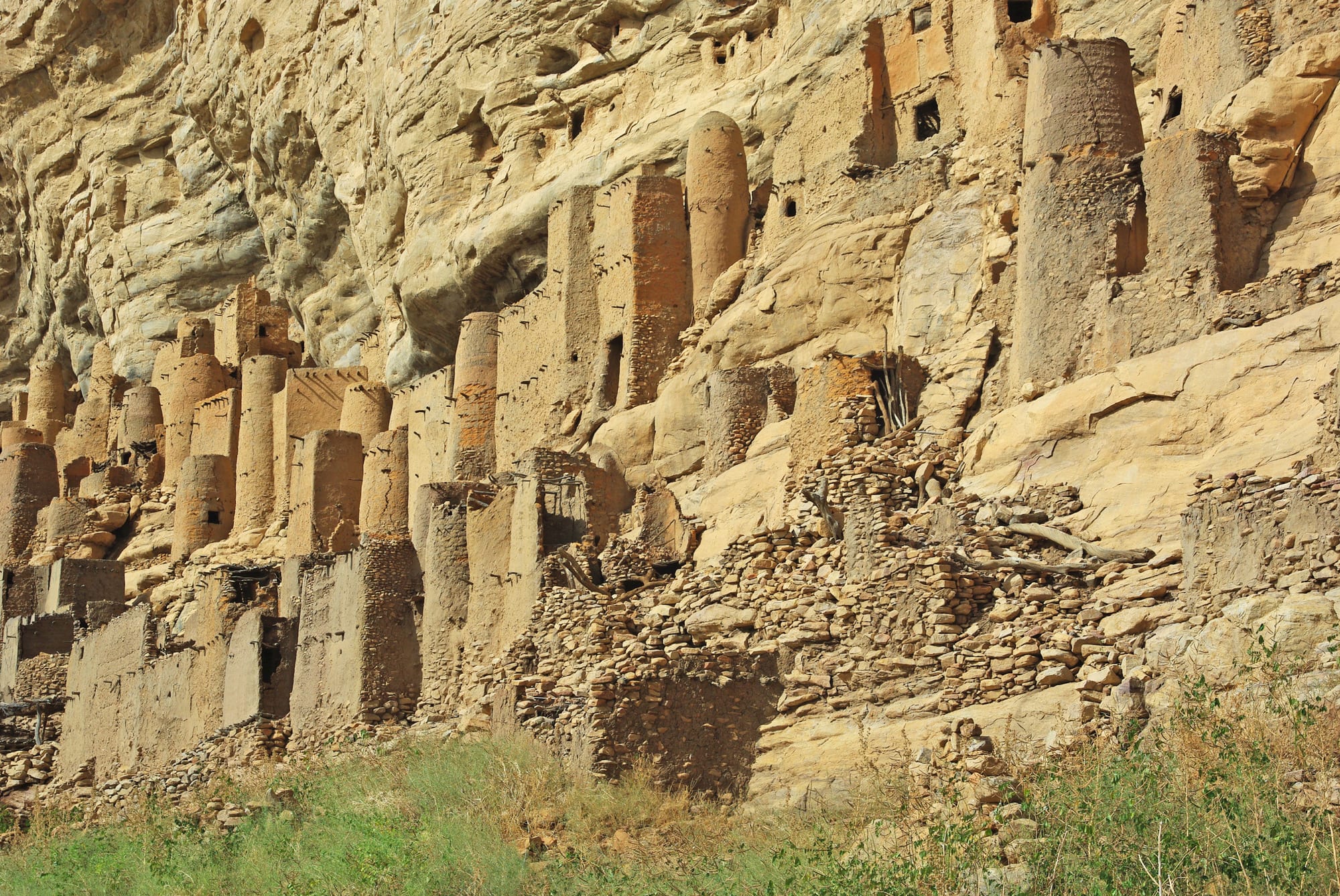 A cluster of mud houses and pointed straw-roofed granaries against a cliff face