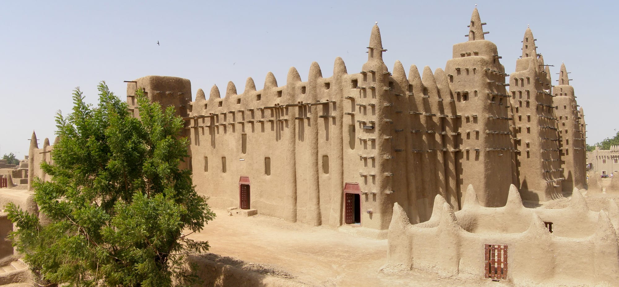A large mud mosque facade with pointed towers and rows of wooden beams jutting from the walls