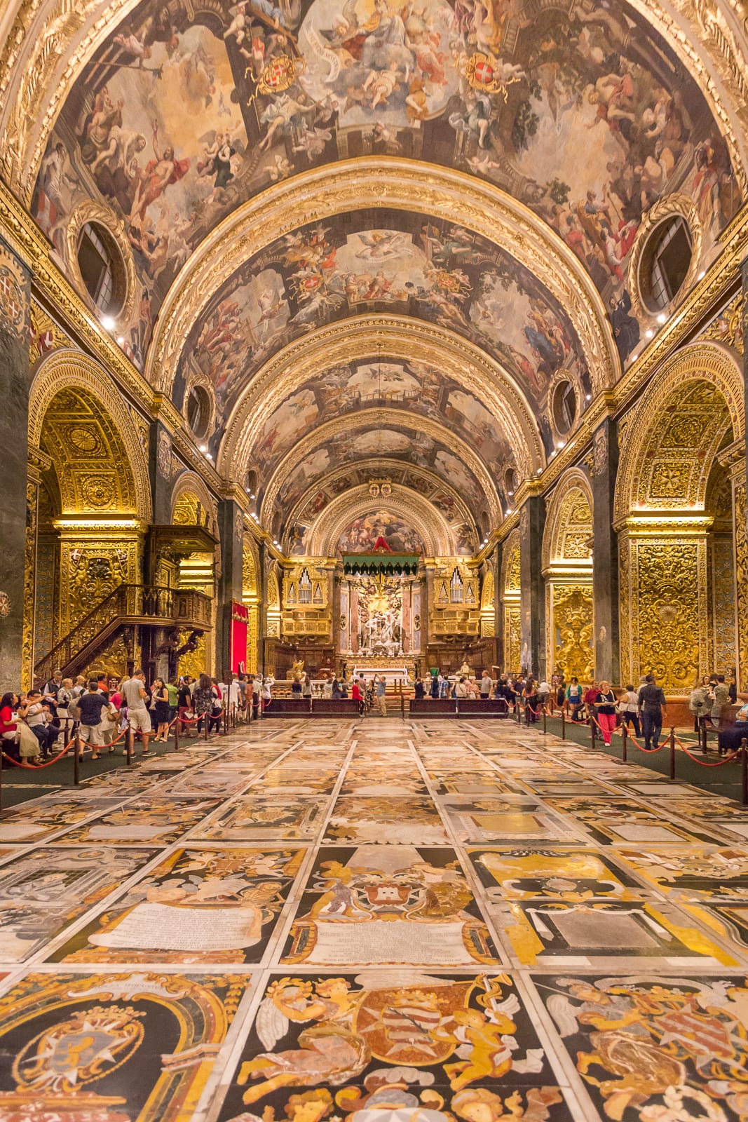 An ornately gilded baroque church interior with a marble inlaid floor of tombstones
