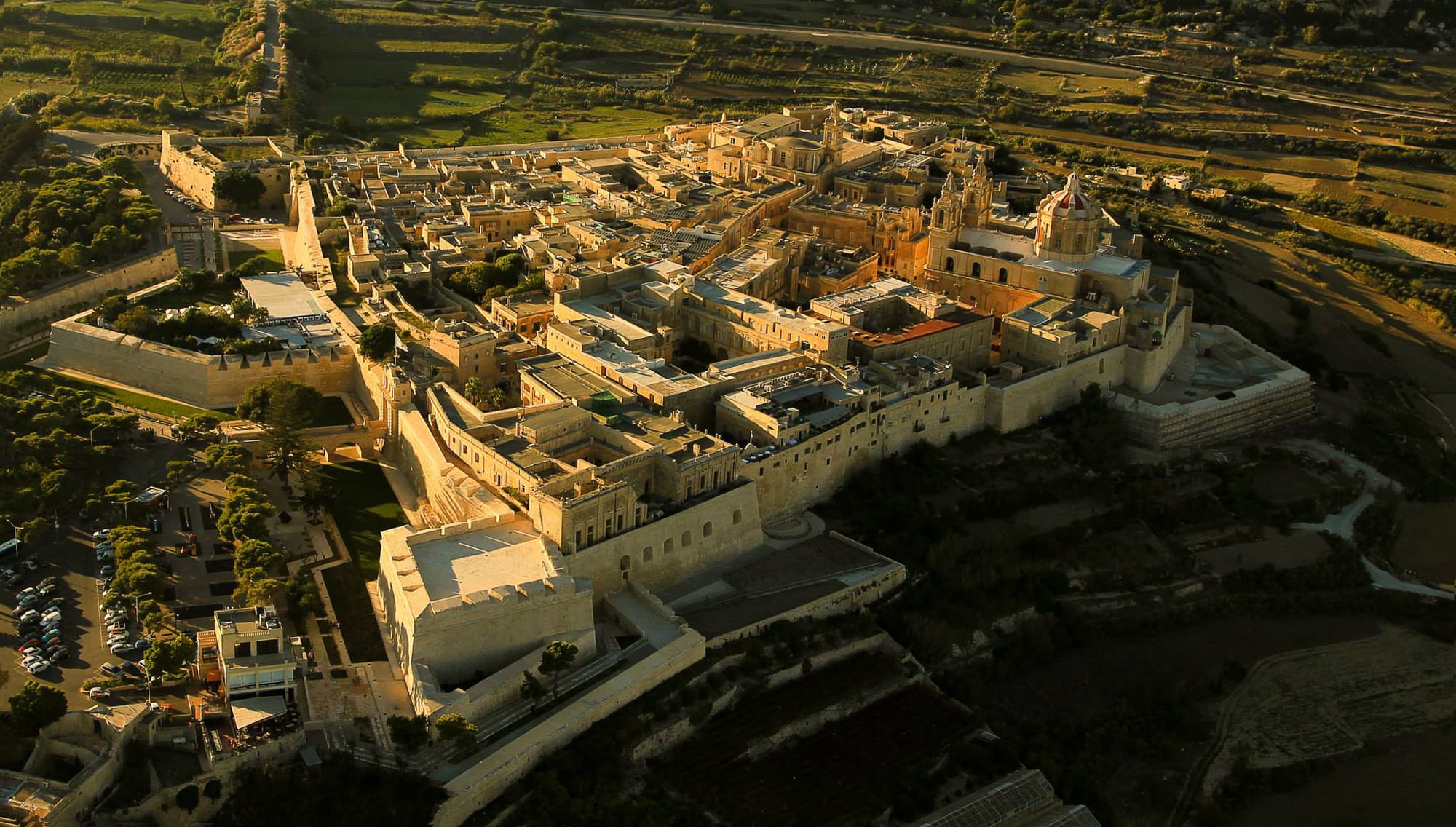 A walled honey-coloured medieval city with a cathedral dome, seen at dusk