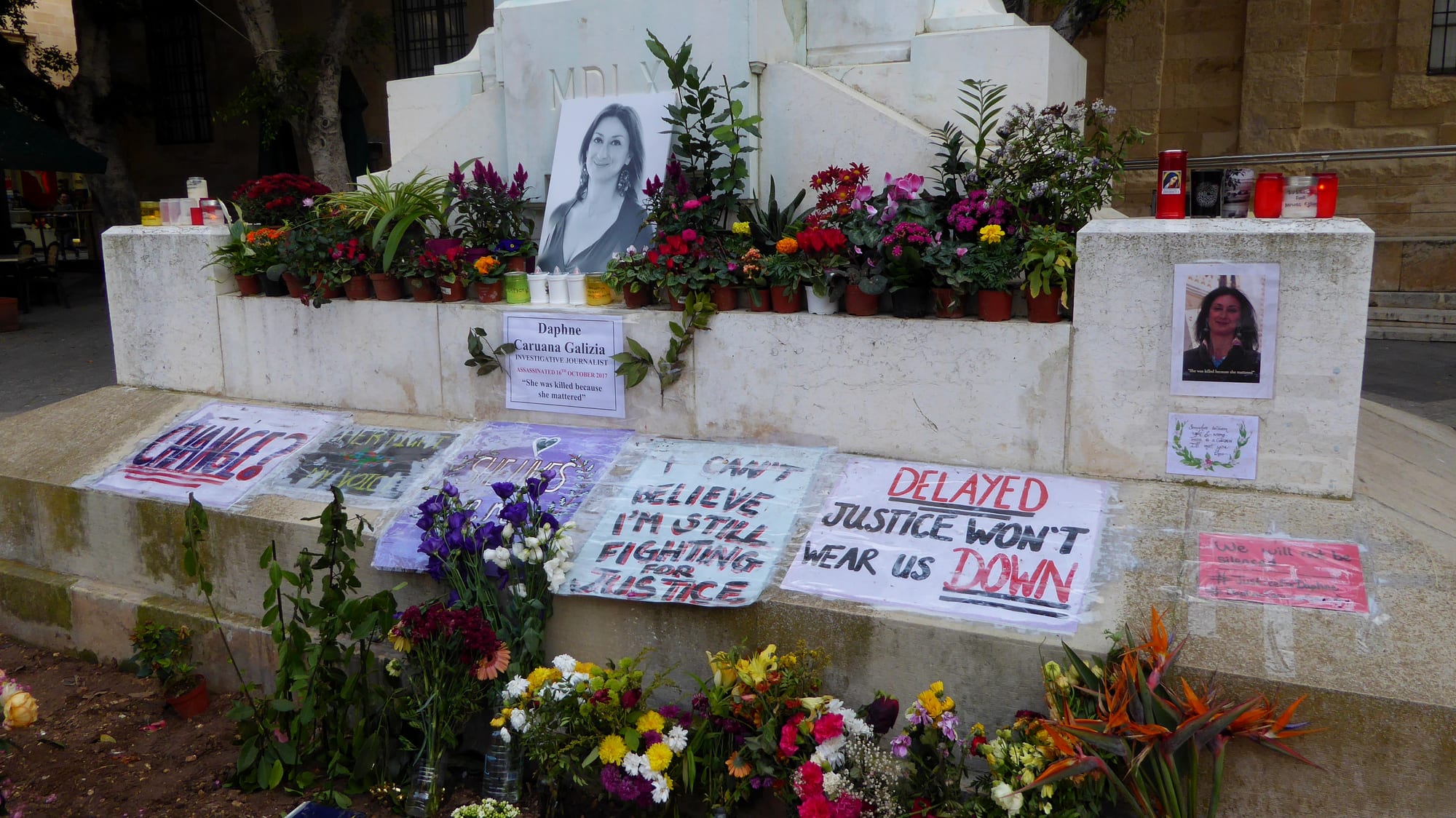 A makeshift protest memorial of flowers, candles and photographs at the foot of a monument in Valletta