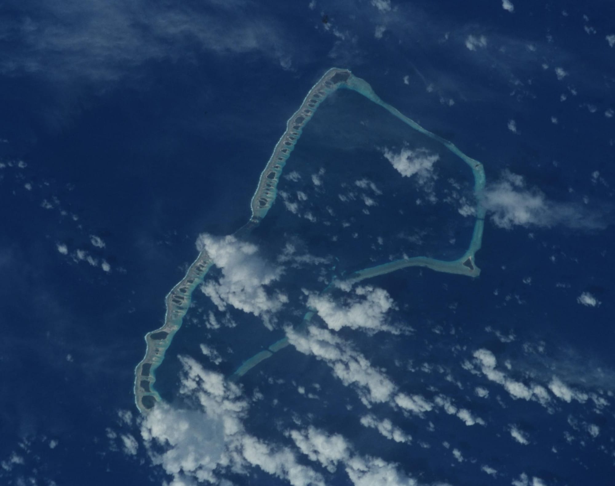 A long, thin coral atoll ringed by reef, seen from orbit