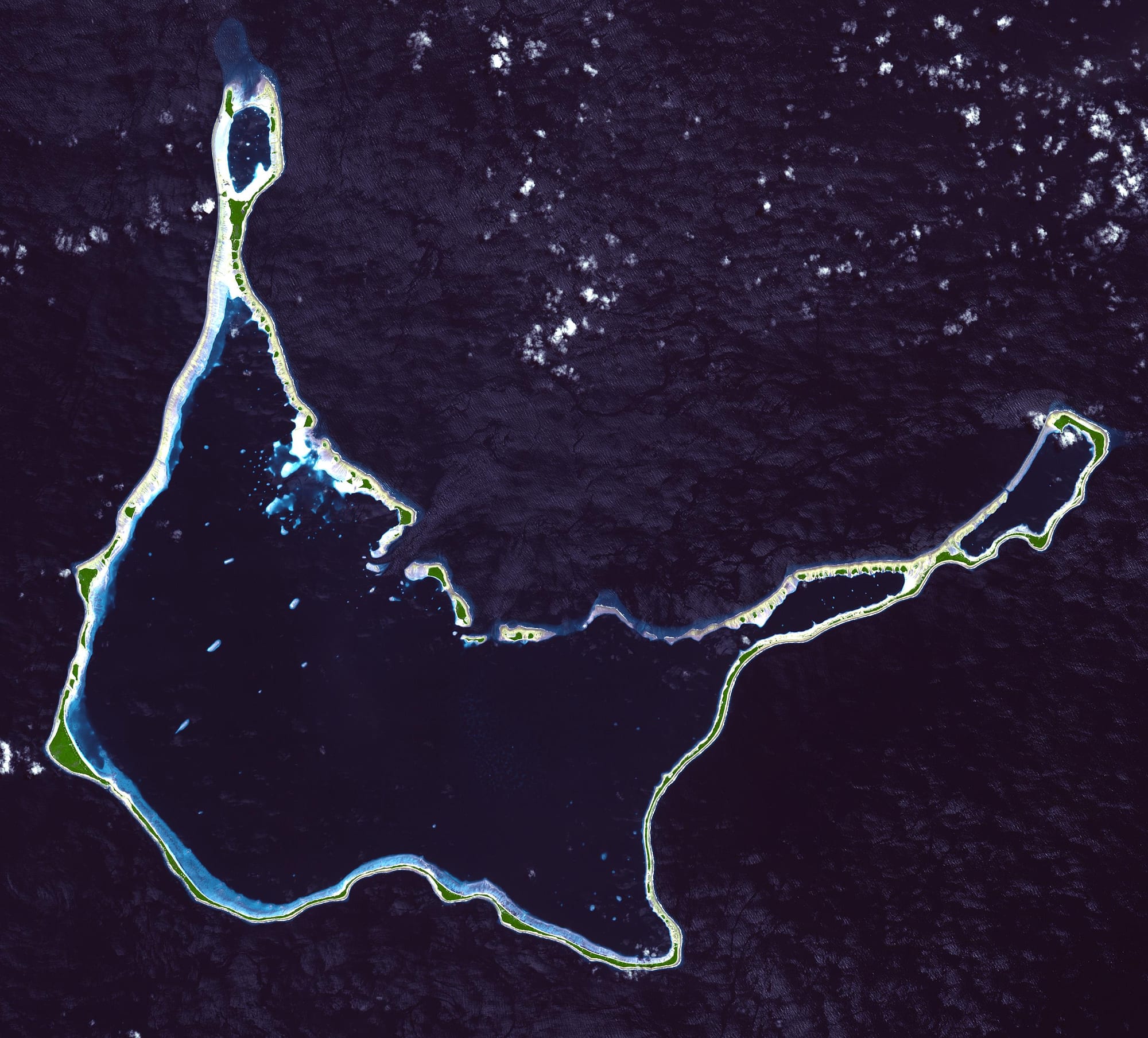 A satellite view of a narrow coral atoll enclosing a turquoise lagoon