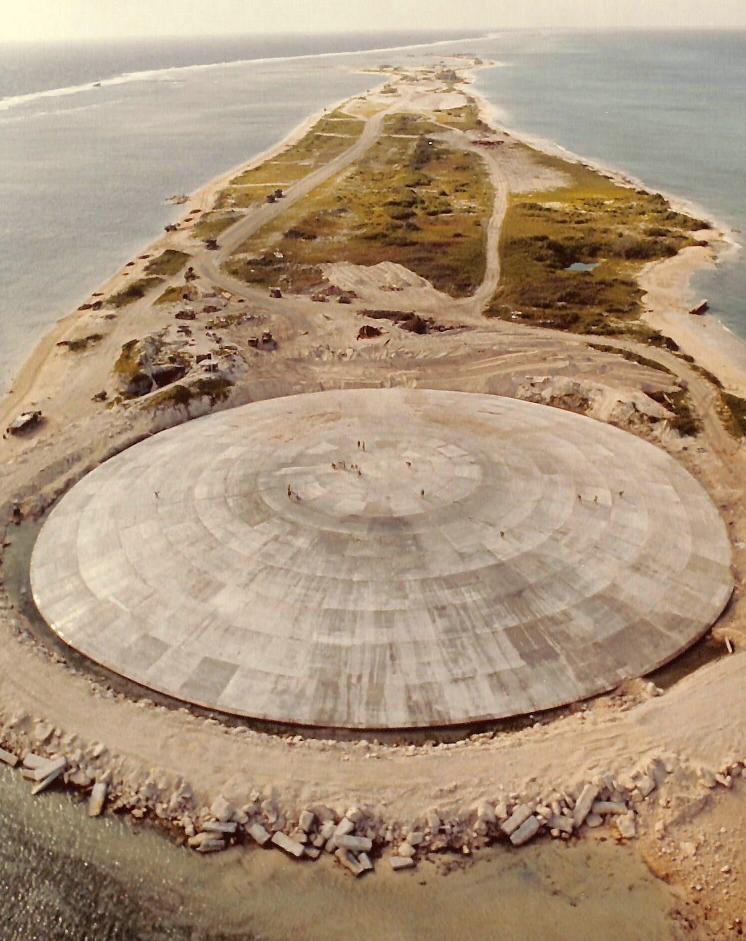 A large low concrete dome covering a former test crater on a bare coral island