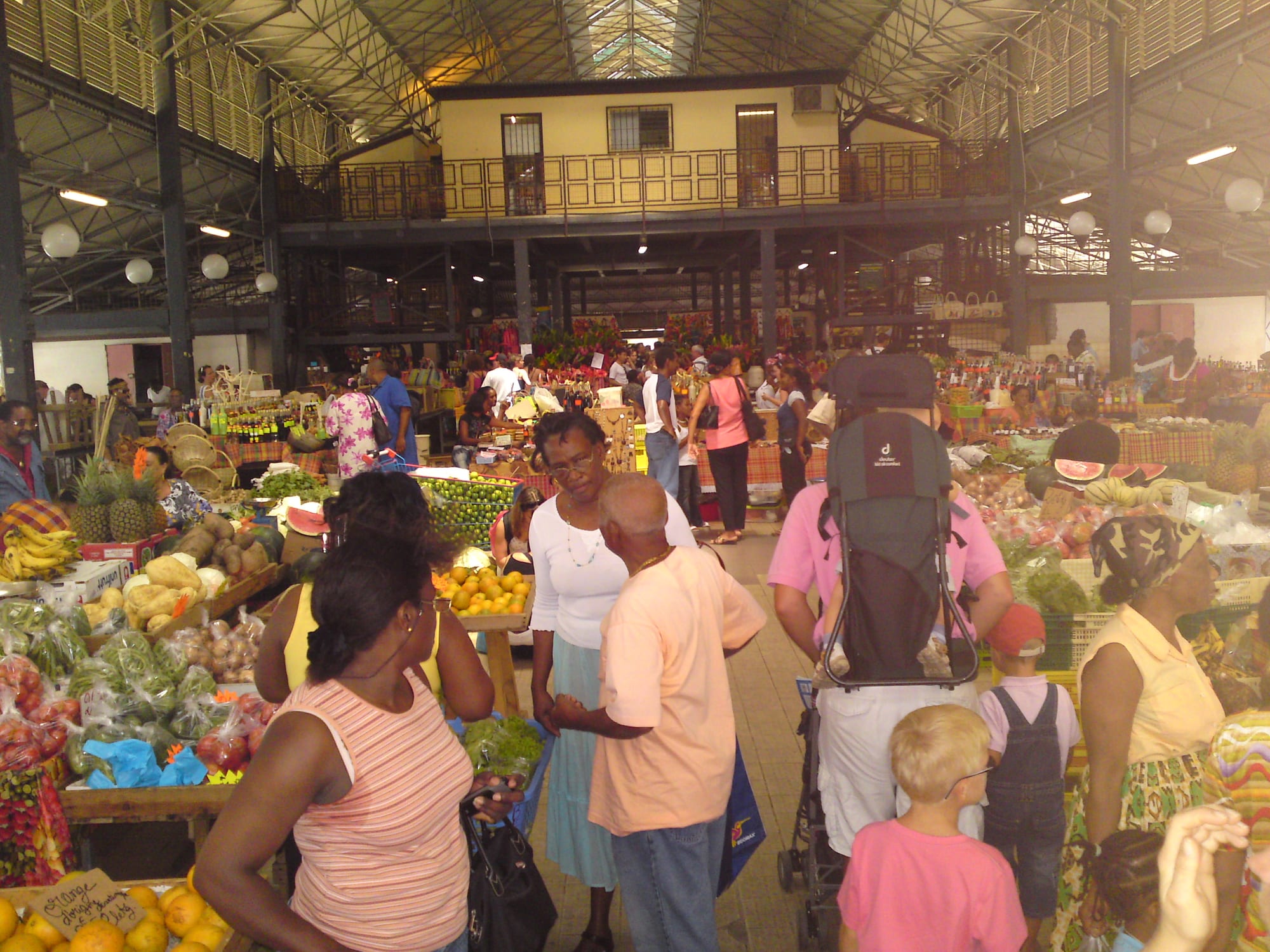 Shoppers and vendors among stalls of fruit and vegetables inside the covered Grand Marché in Fort-de-France, under its iron-and-glass roof
