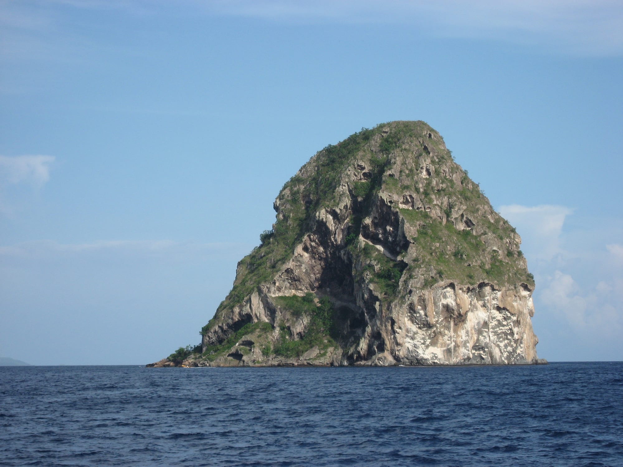 A tall, steep volcanic rock islet rising from the sea off a coastline