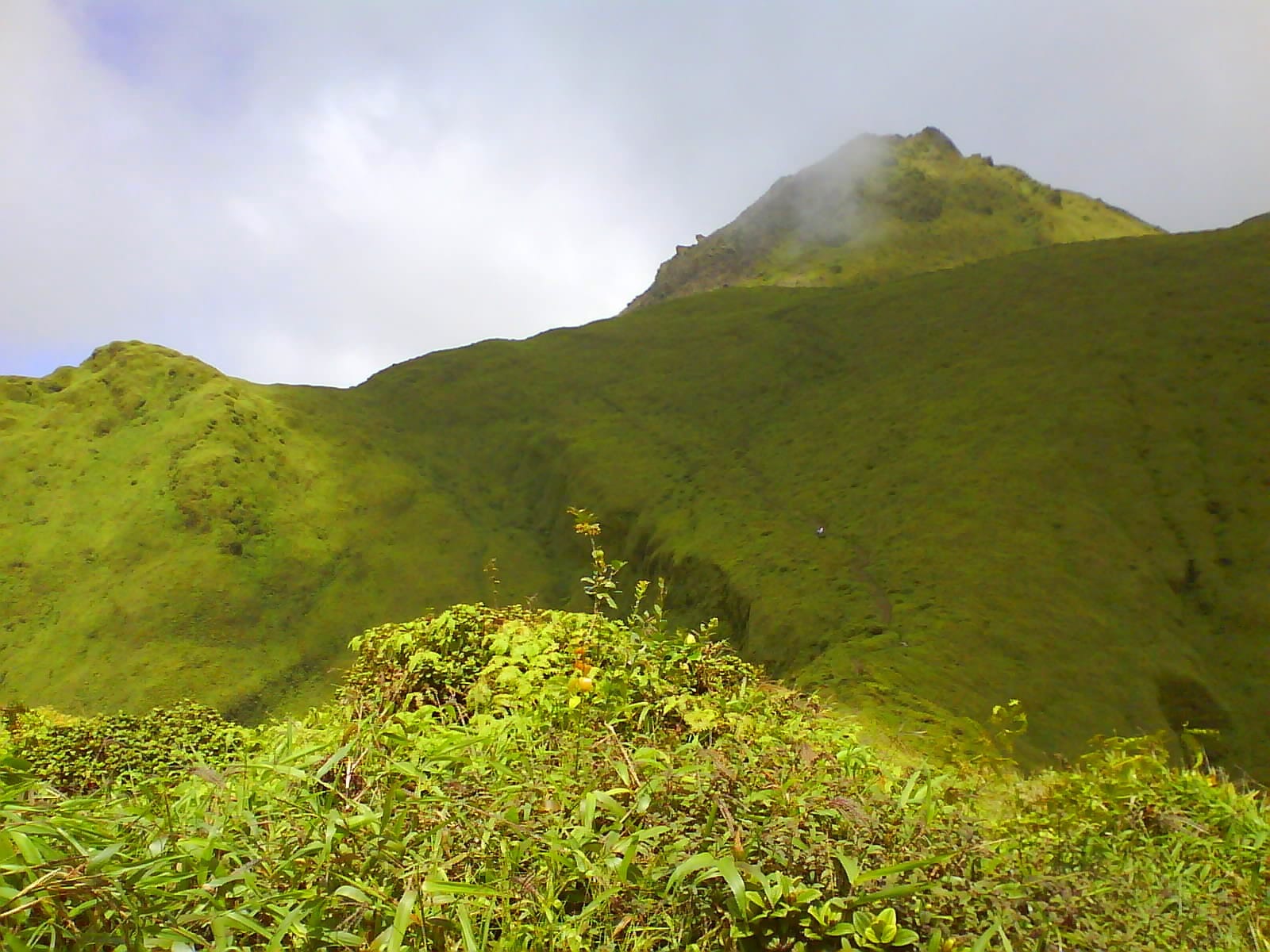 A green volcanic peak with cloud drifting across its summit