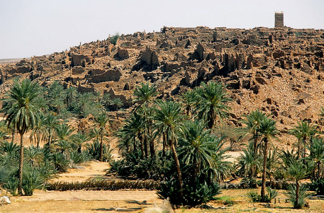 Ruined stone buildings of an old hilltop town overlooking a palm-filled desert valley