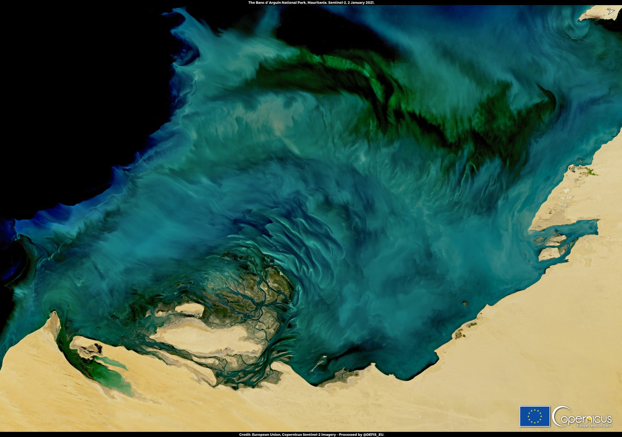 A satellite view of shallow turquoise coastal waters, sandbanks, and desert coastline