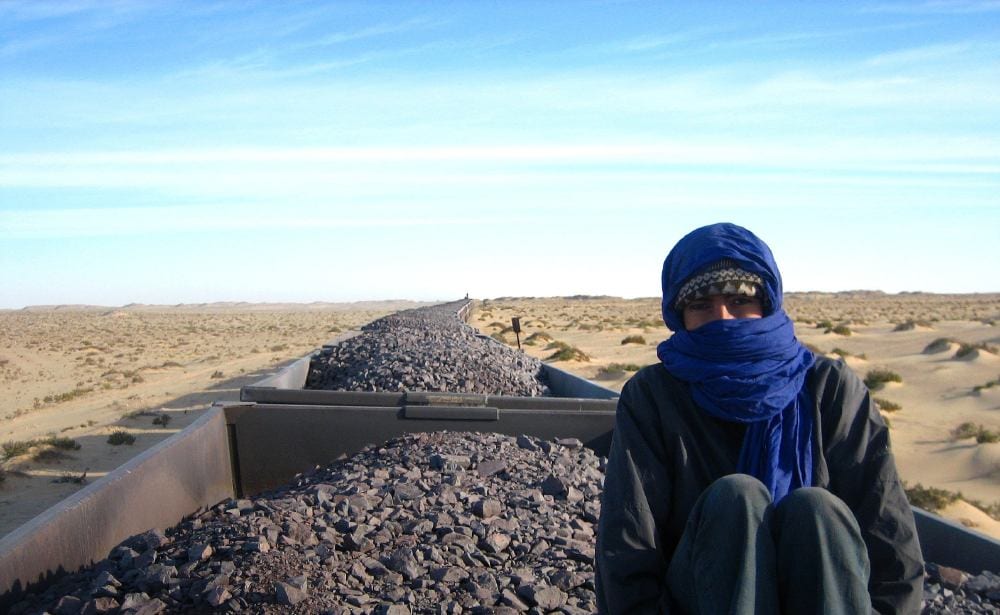 A very long freight train of ore wagons stretching across a flat desert landscape