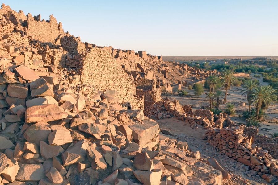 The stone ruins of an old desert town on a rocky slope, with a modern village beyond