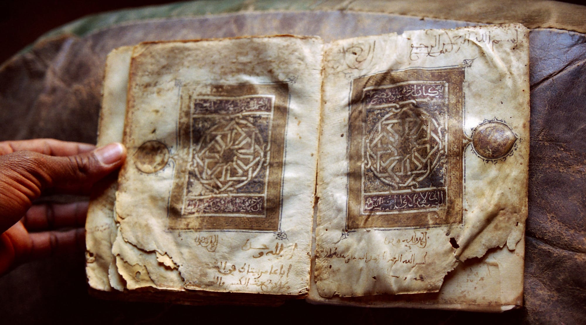 An ancient handwritten Quran with ornate script, held open in a family library at Chinguetti