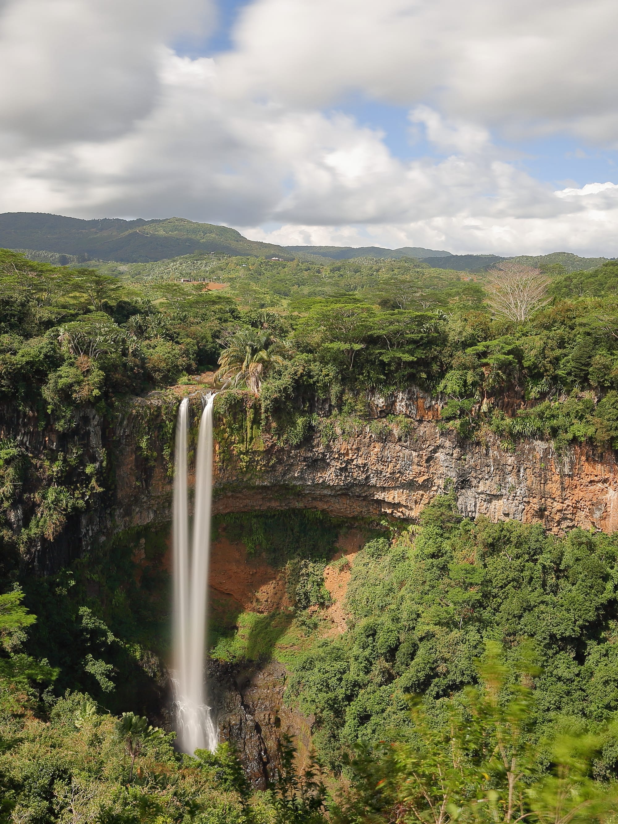A tall single waterfall dropping into a forested gorge