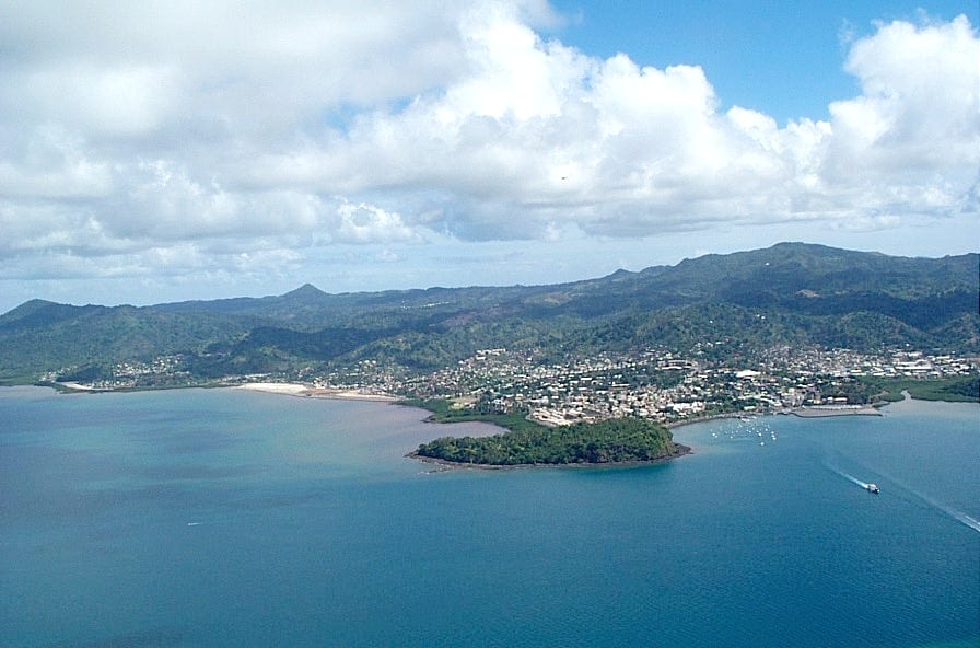 An aerial view of Mamoudzou on Mayotte's coast, houses and hills wrapped around a blue lagoon with small boats near the shore