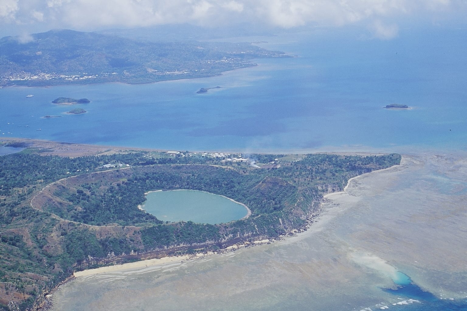 A round, bright green lake filling a volcanic crater surrounded by dry hills