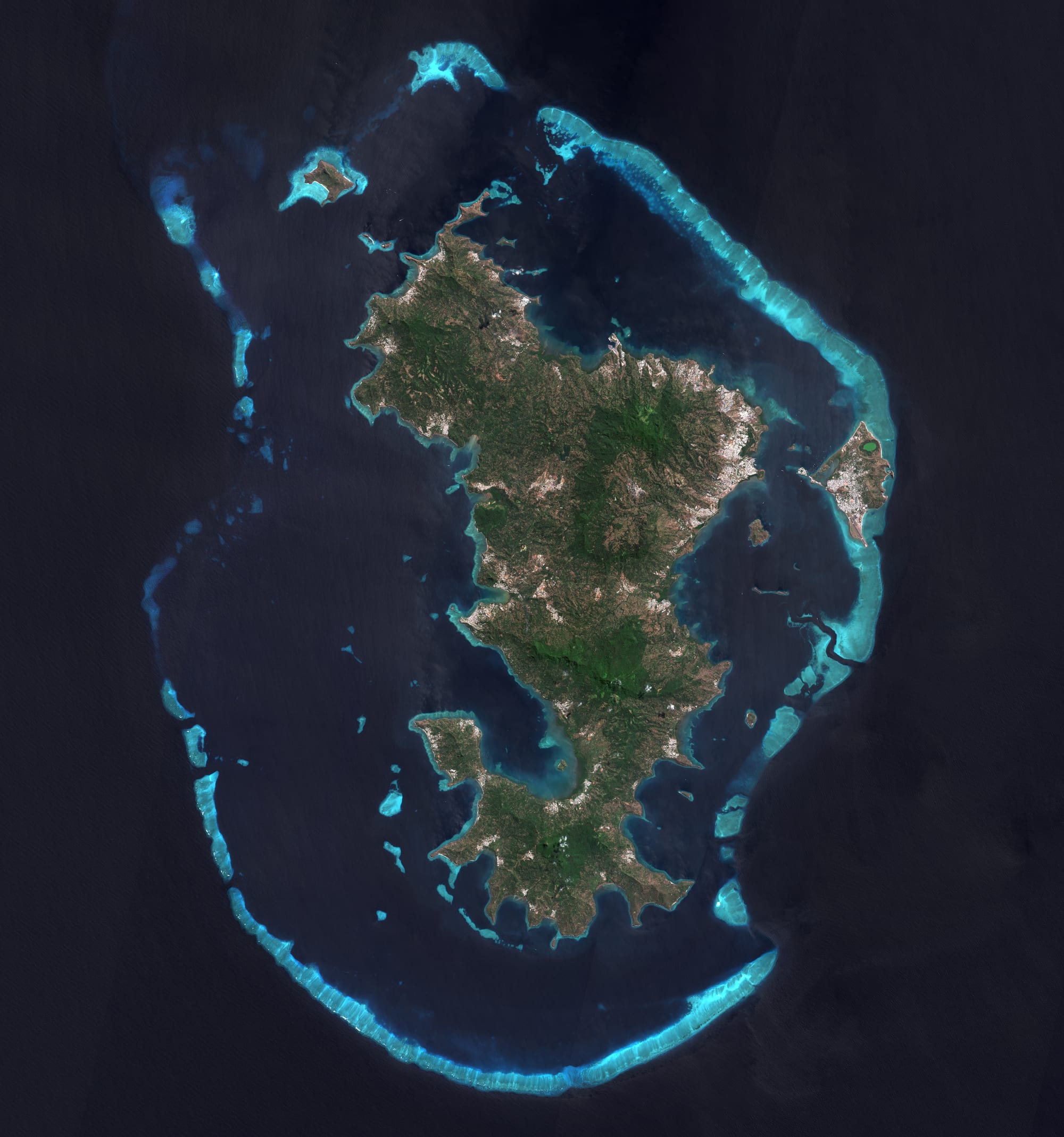 A satellite view of a green island surrounded by one of the world's largest coral lagoons