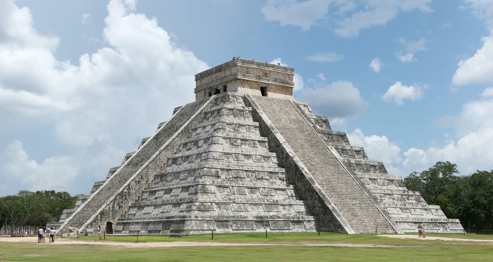 A stepped stone pyramid with a temple on top, standing in a grassy plaza