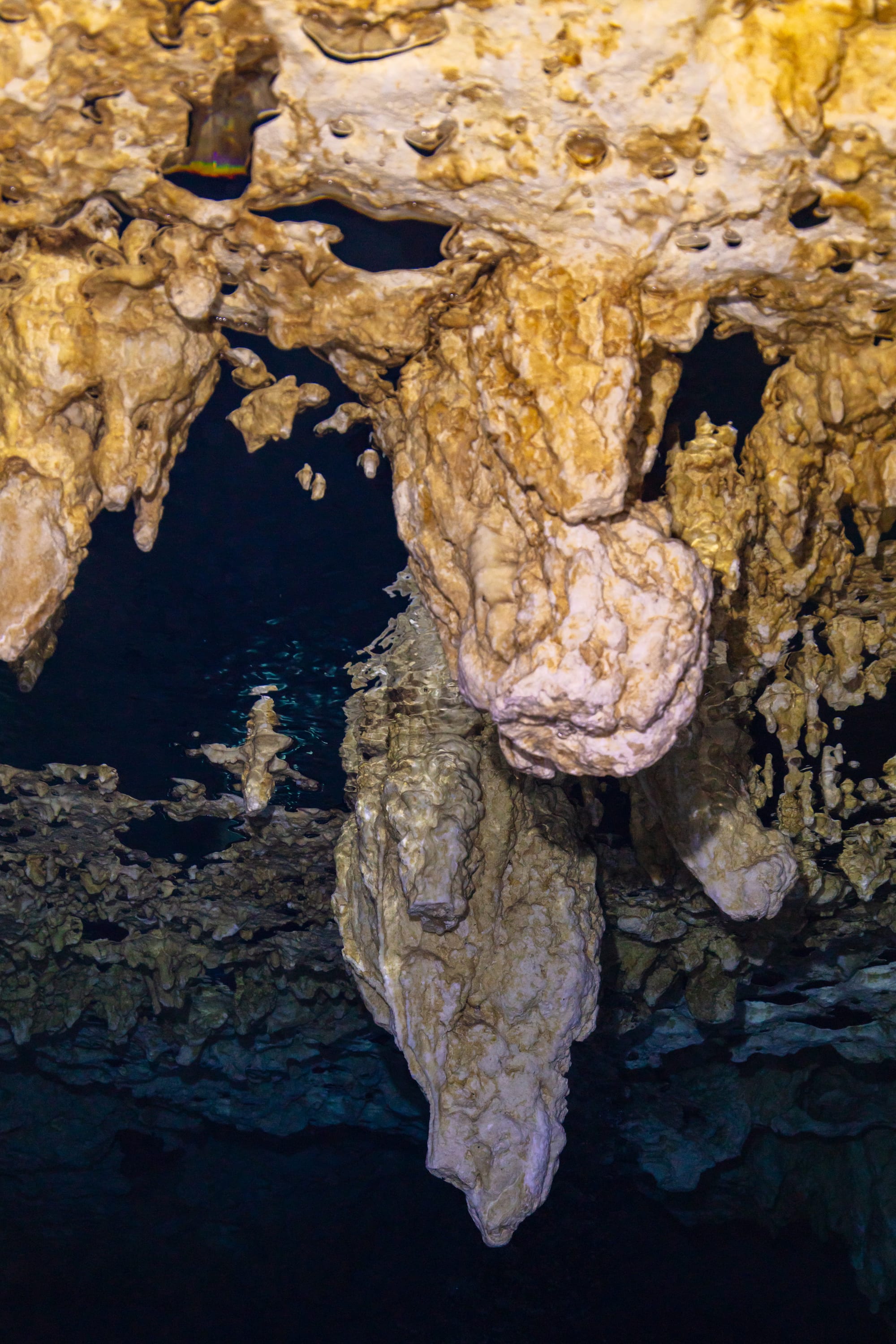 Dramatic limestone stalactite formations hanging over dark cave water