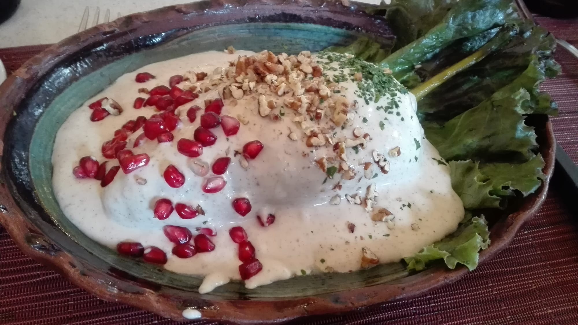 Poblano peppers stuffed with meat and fruit, topped with a white walnut cream sauce and pomegranate seeds