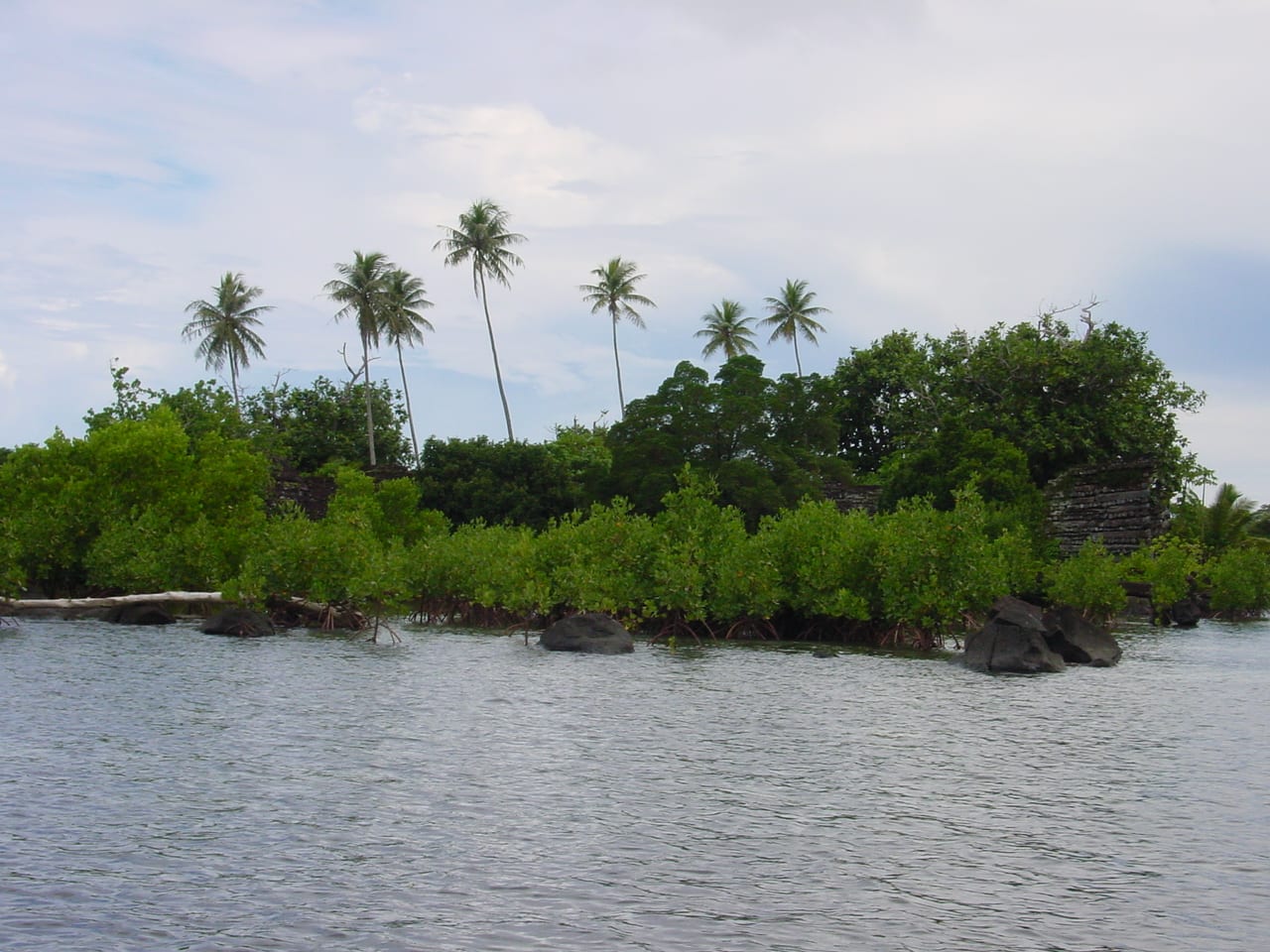 Ruined black basalt-log walls rising from a mangrove-lined lagoon