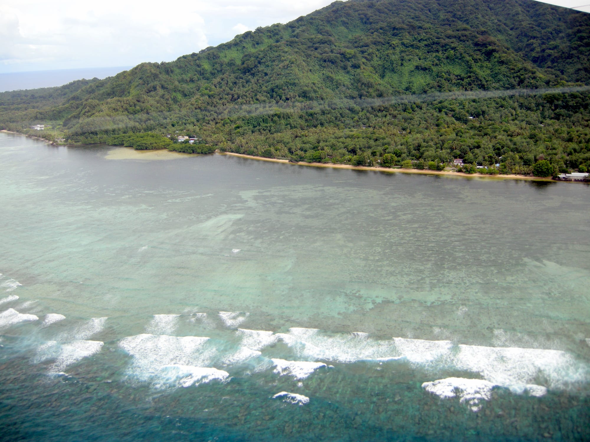 A lush green mountainous island rising from the sea, ringed by reef