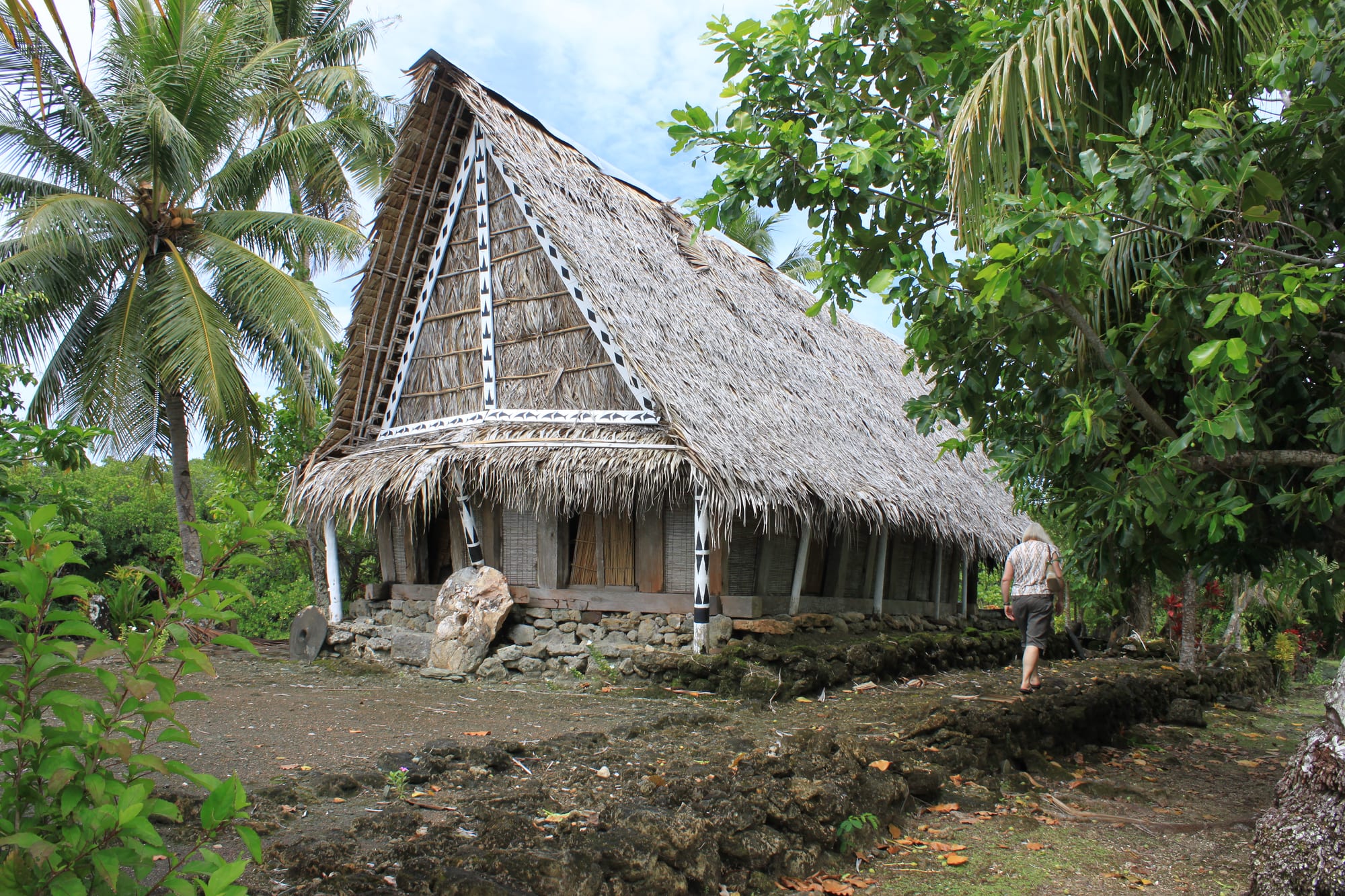 A traditional Yap men's house with a steep thatched roof and carved supporting posts, set among palm trees