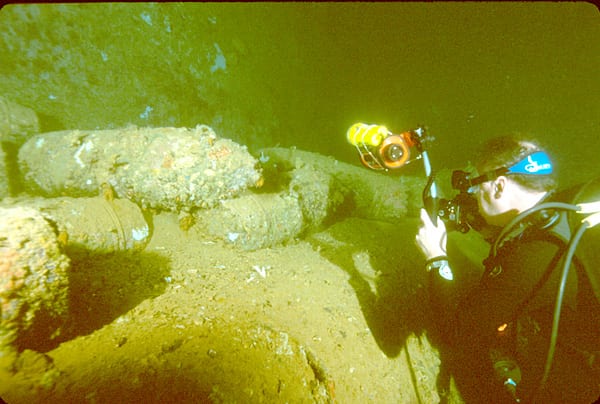 A scuba diver with a camera hovering over stacked shells in the hold of a sunken ship