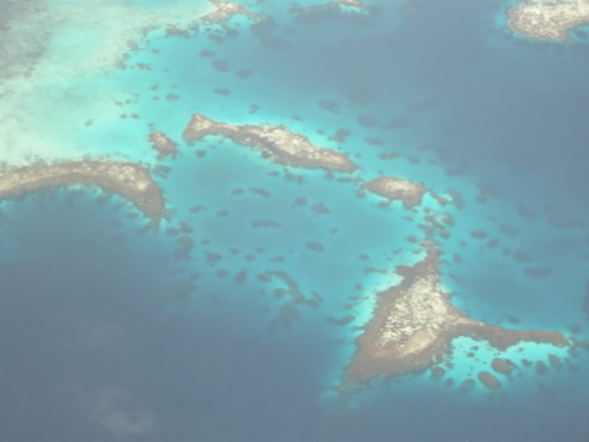 An aerial view of a barrier reef enclosing a wide blue lagoon dotted with islands