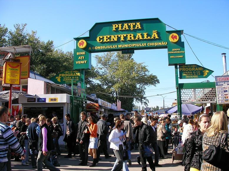 A crowd of shoppers passing beneath the green entrance arch of Piata Centrala market in Chisinau