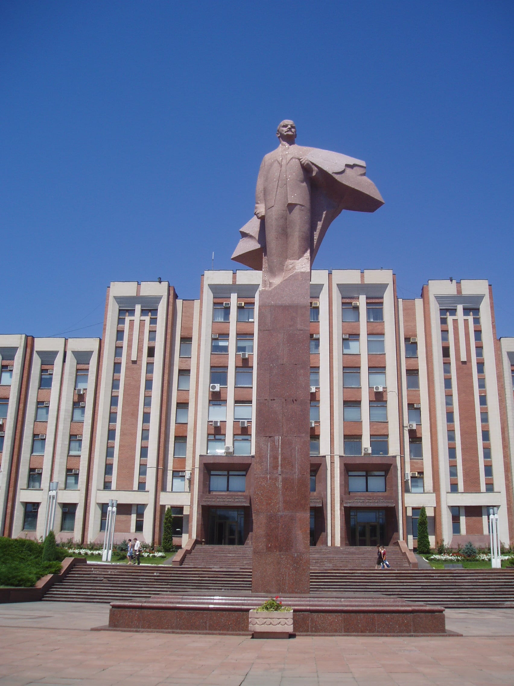 A statue of Lenin on a tall plinth in front of a Soviet-style government building