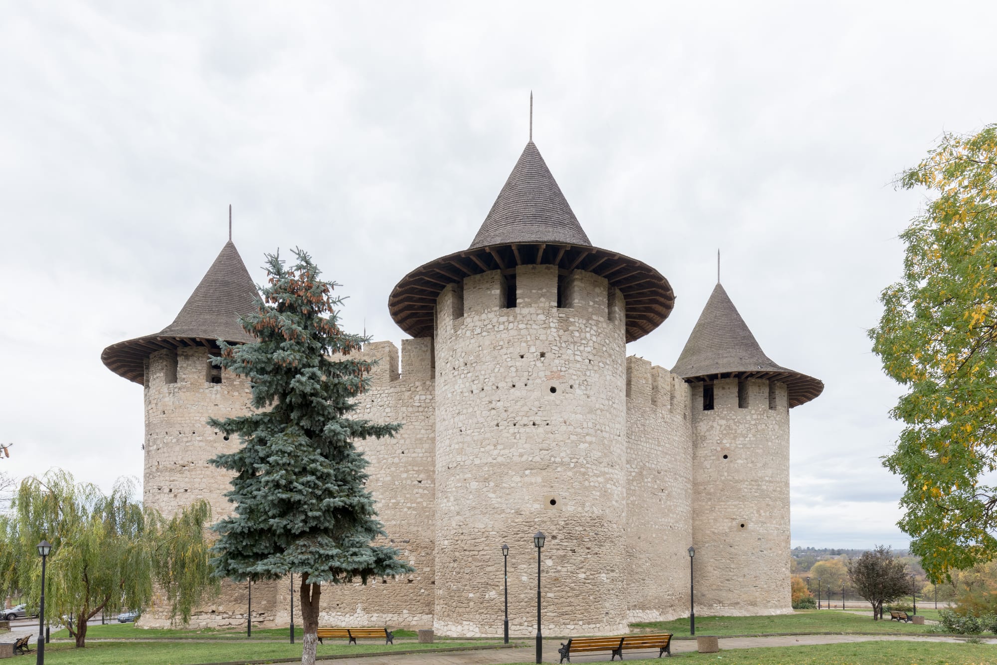 A round stone medieval fortress with cylindrical towers beside a river