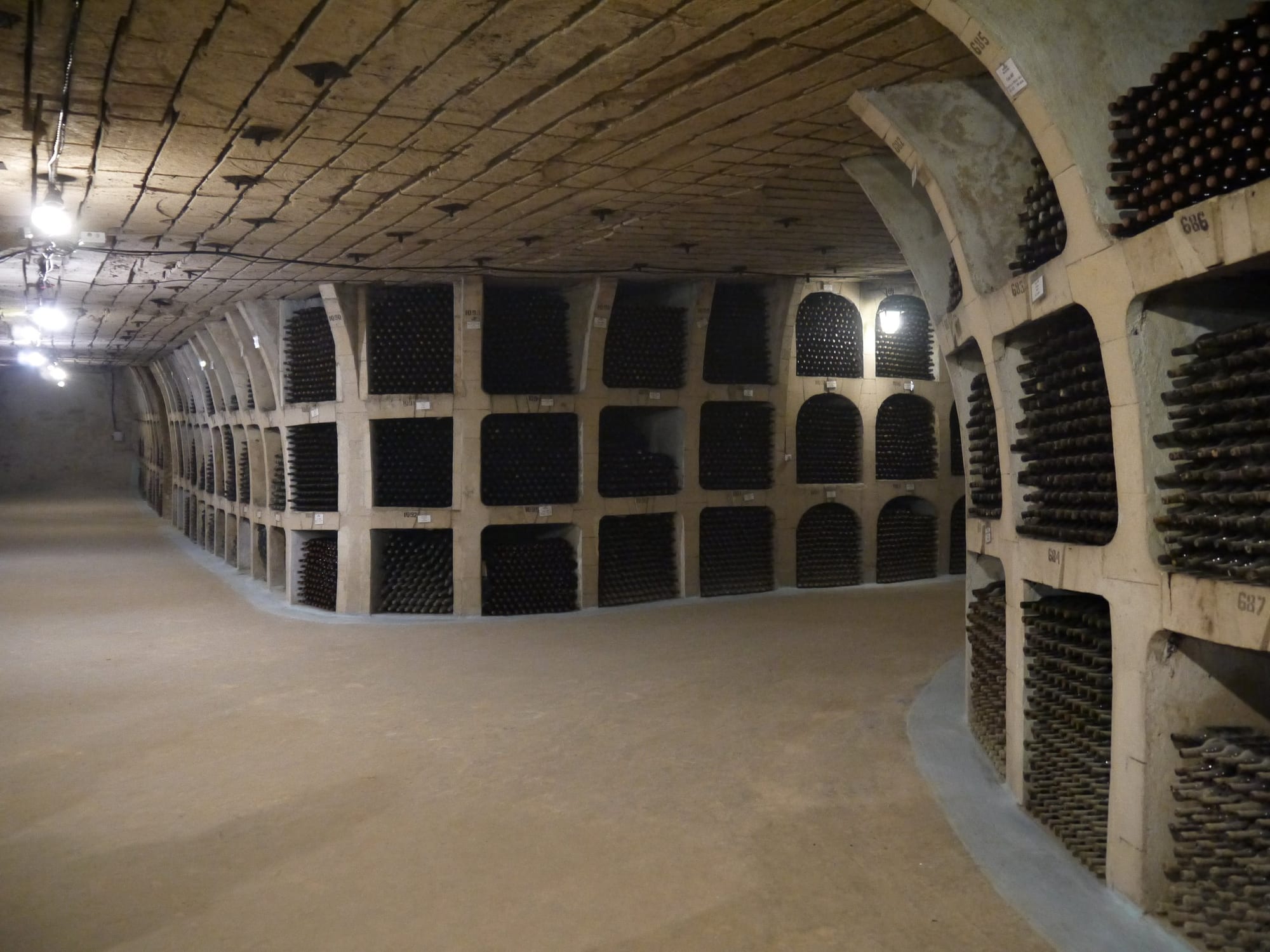 Rows of wine bottles stacked in niches lining an underground limestone tunnel
