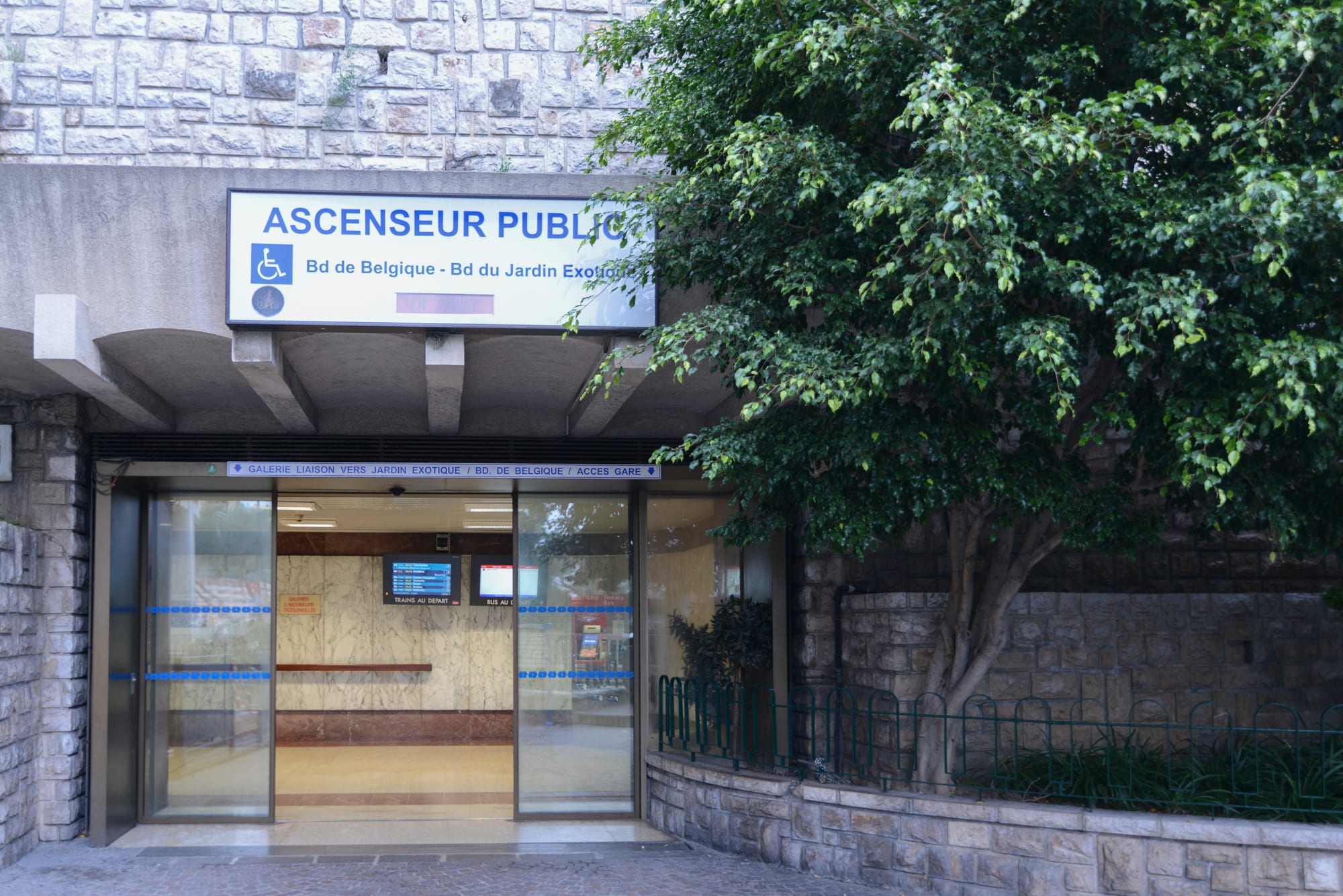 The glass-fronted entrance to a public lift, signposted Ascenseur Public, leading down to Monaco's railway station