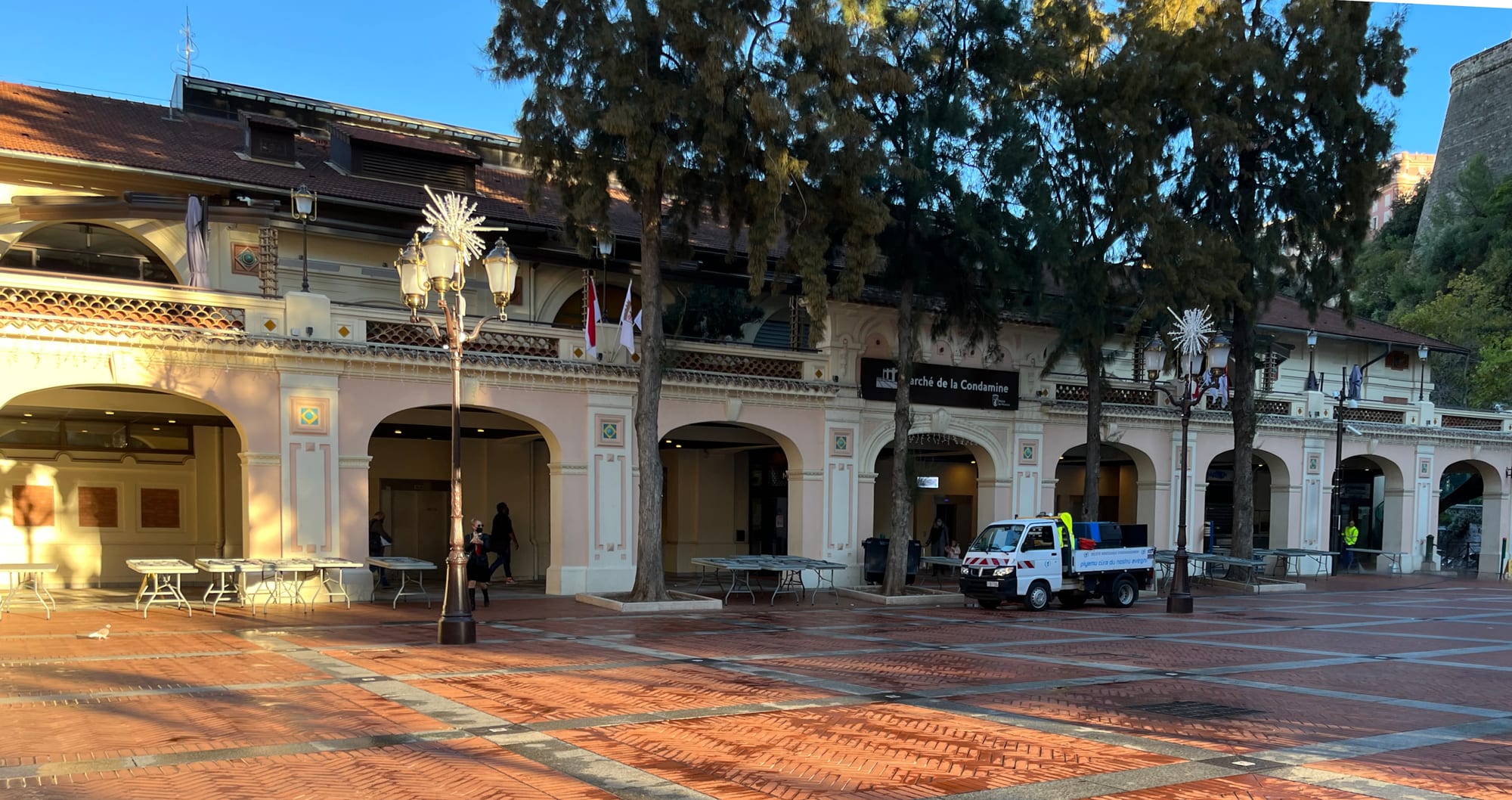 The covered market hall of the Marché de la Condamine in Monaco, seen across an empty paved square with café tables
