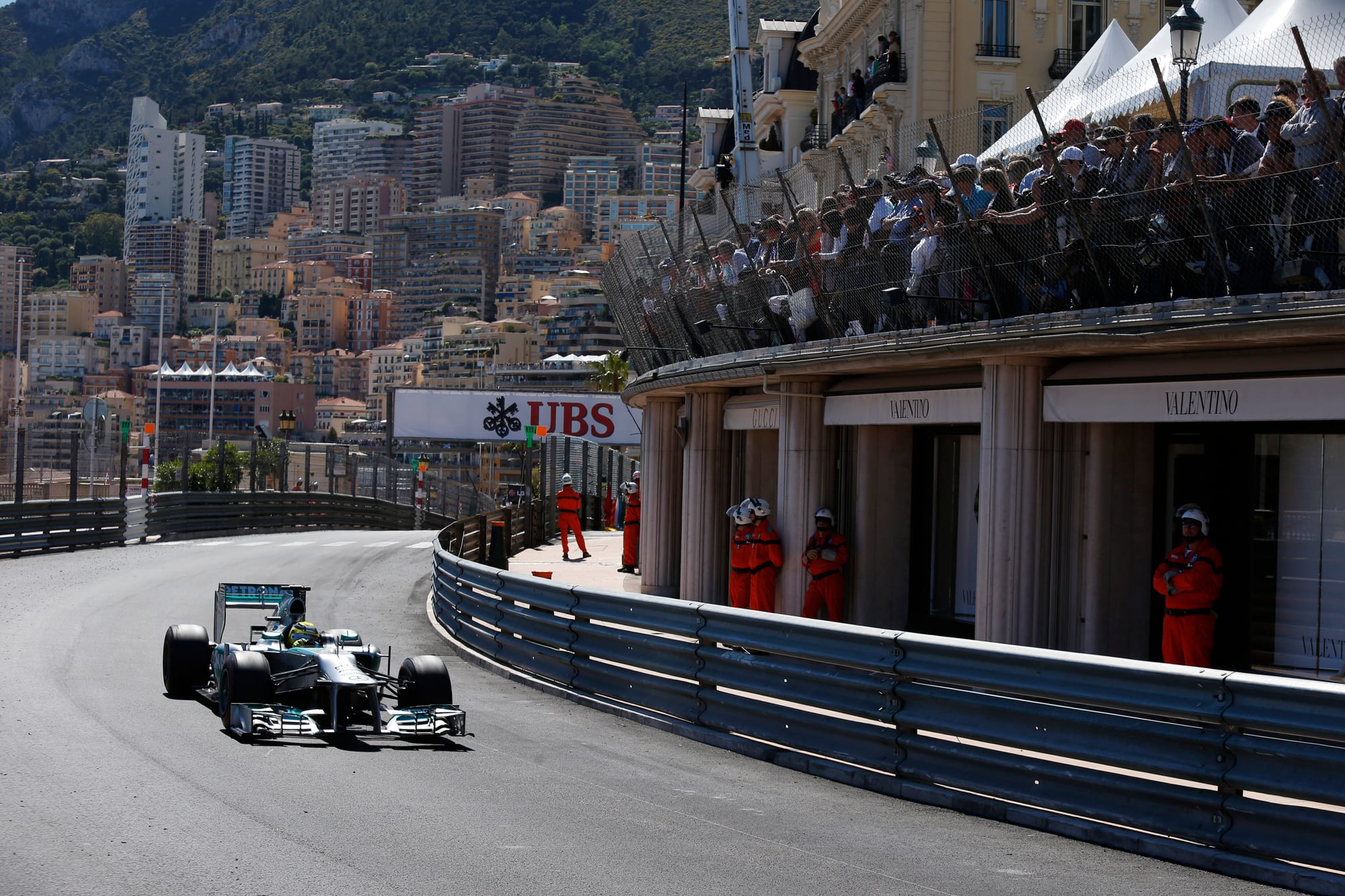 A Formula 1 car racing through a tight street circuit lined with crowds and the city behind