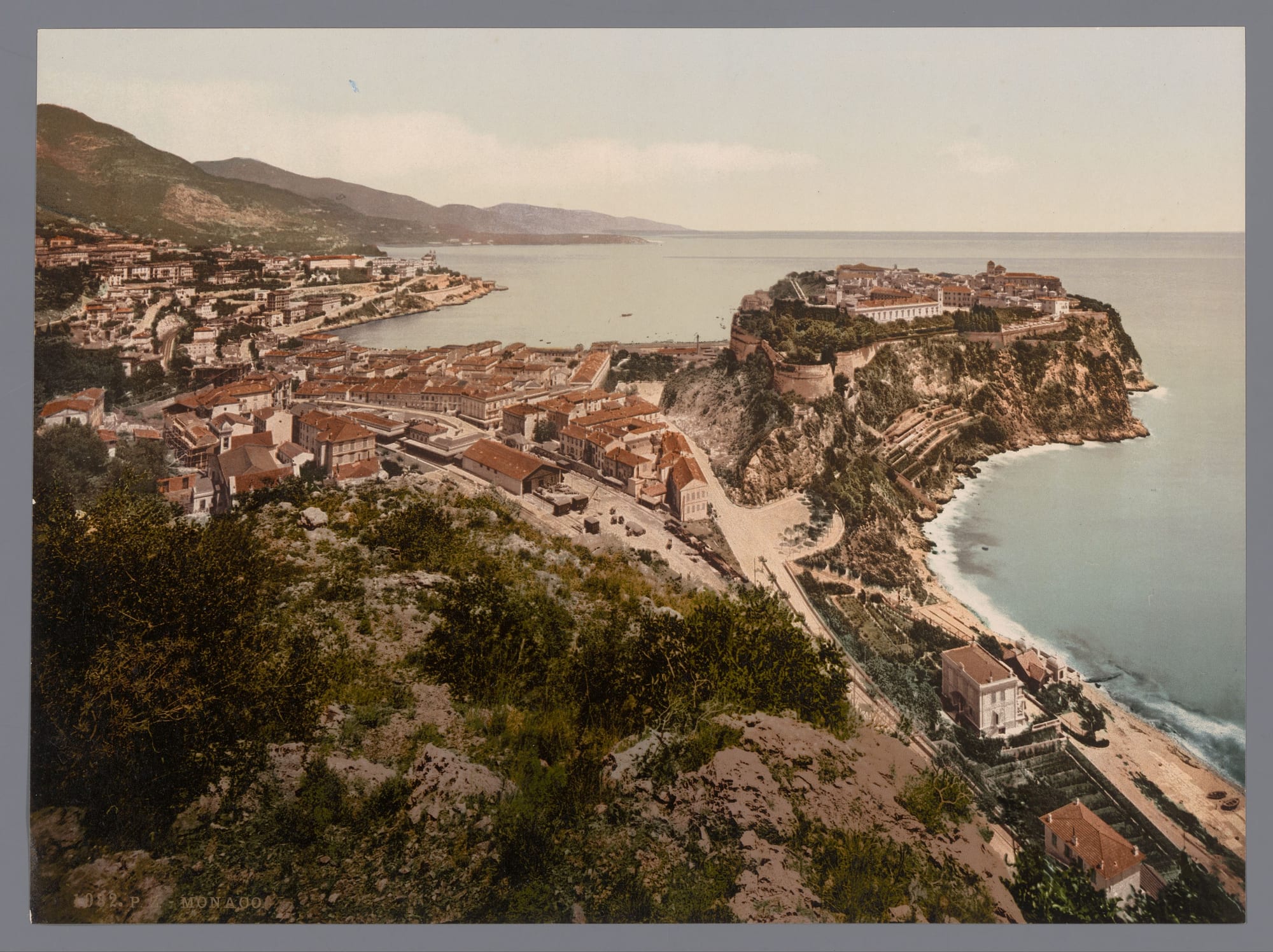 A hand-coloured historic print of a walled town on a steep rocky headland jutting into the sea, with red-roofed houses and a harbour behind it