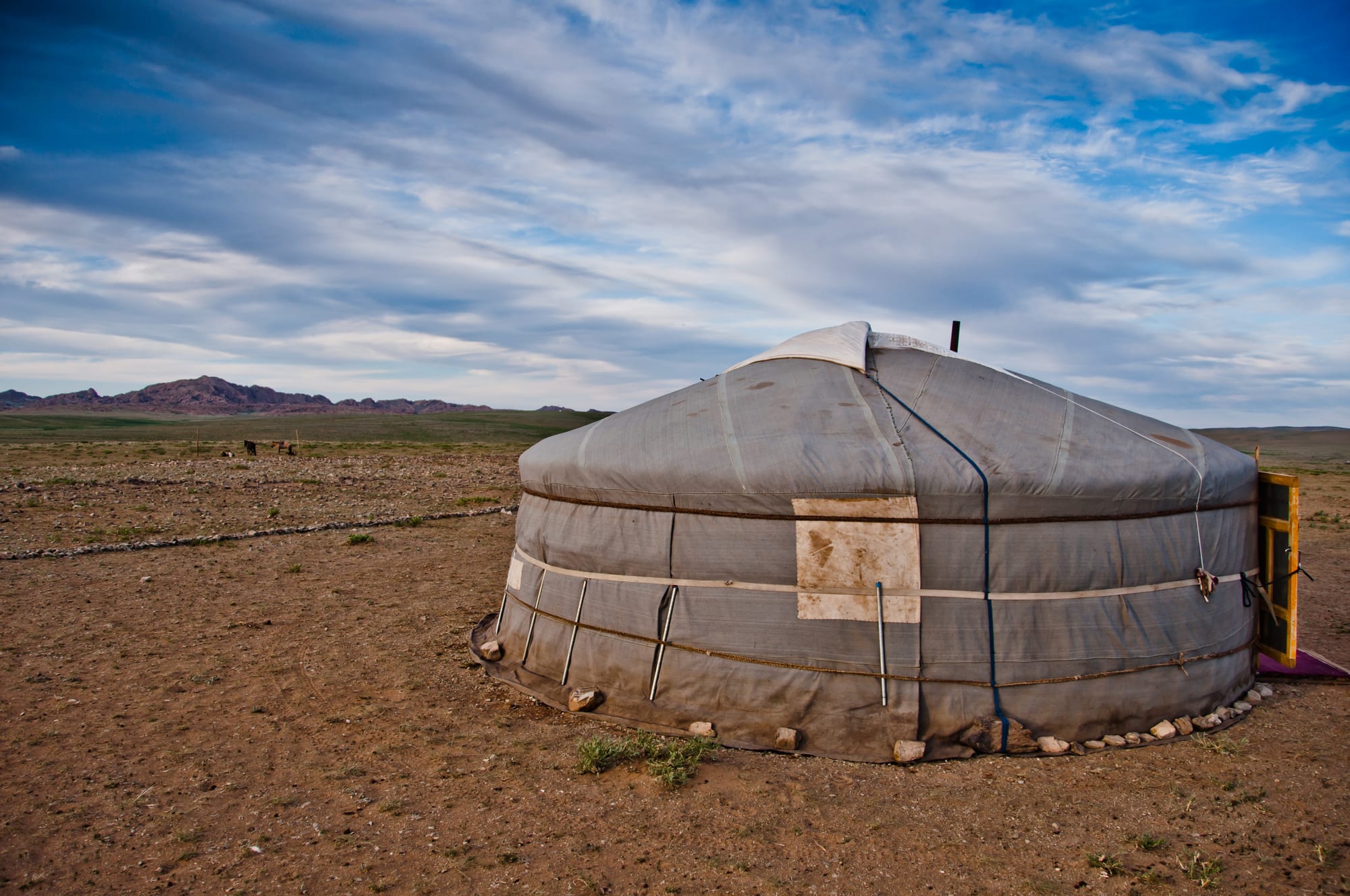 A round white felt tent on open steppe grassland with mountains behind