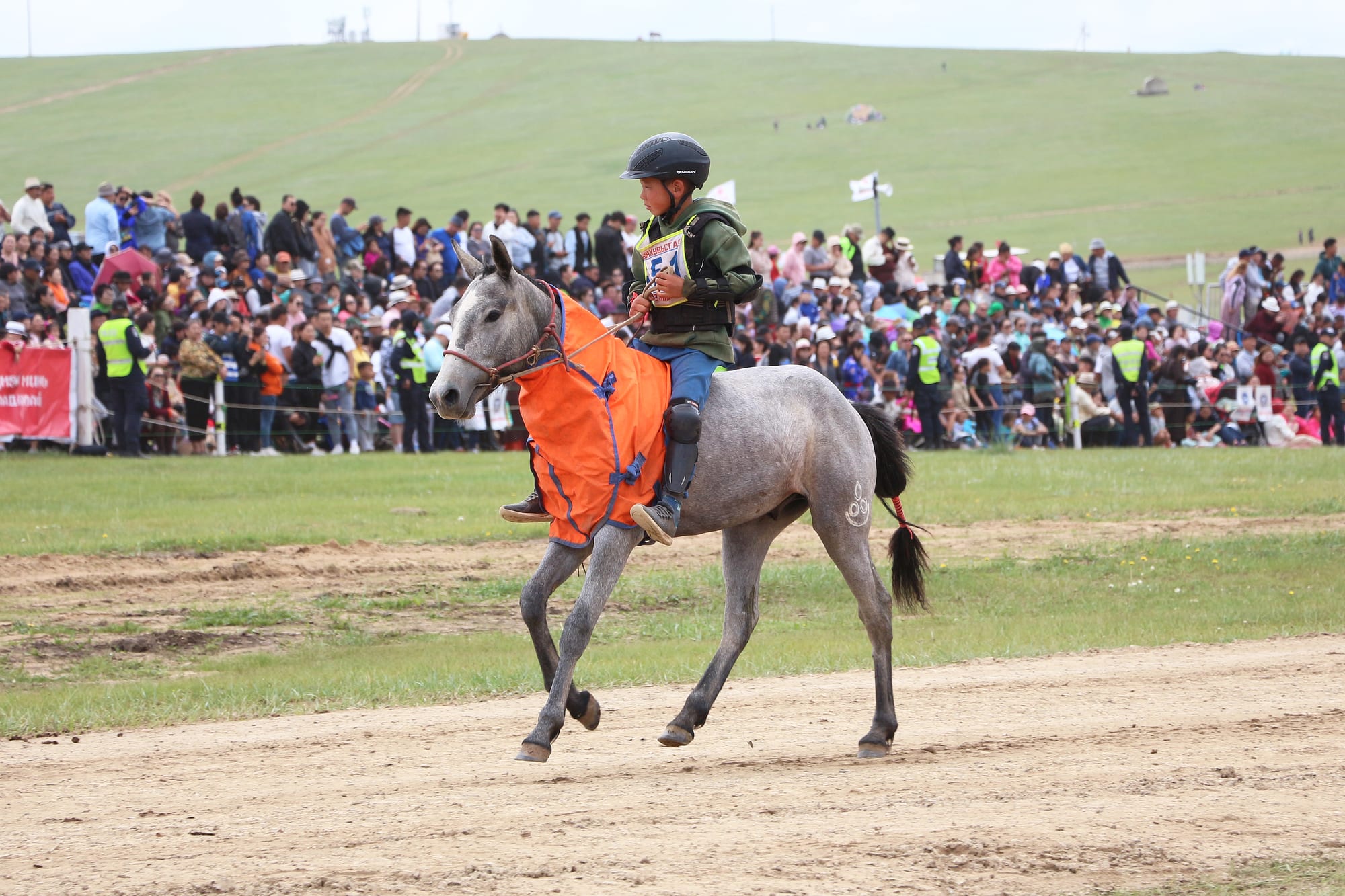 Young jockeys racing horses across open grassland during a festival