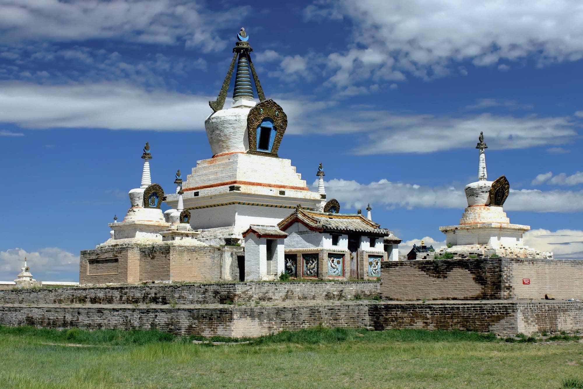 A walled monastery complex with white stupas and pagoda-roofed temples